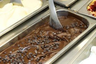 Una vaschetta di gelato al cioccolato con gocce di cioccolato e un cucchiaio dentro.