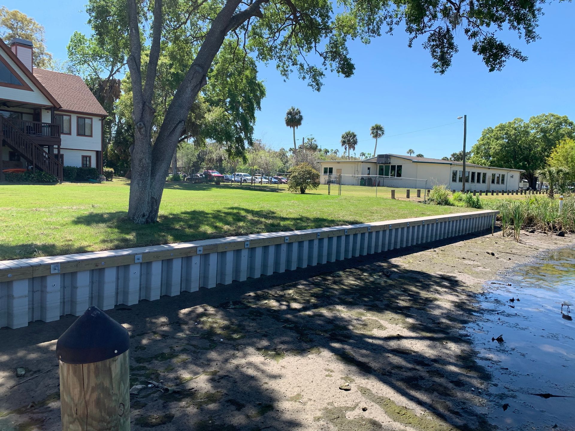 A waterfront view with a concrete retaining wall, grassy area, and buildings on a sunny day.