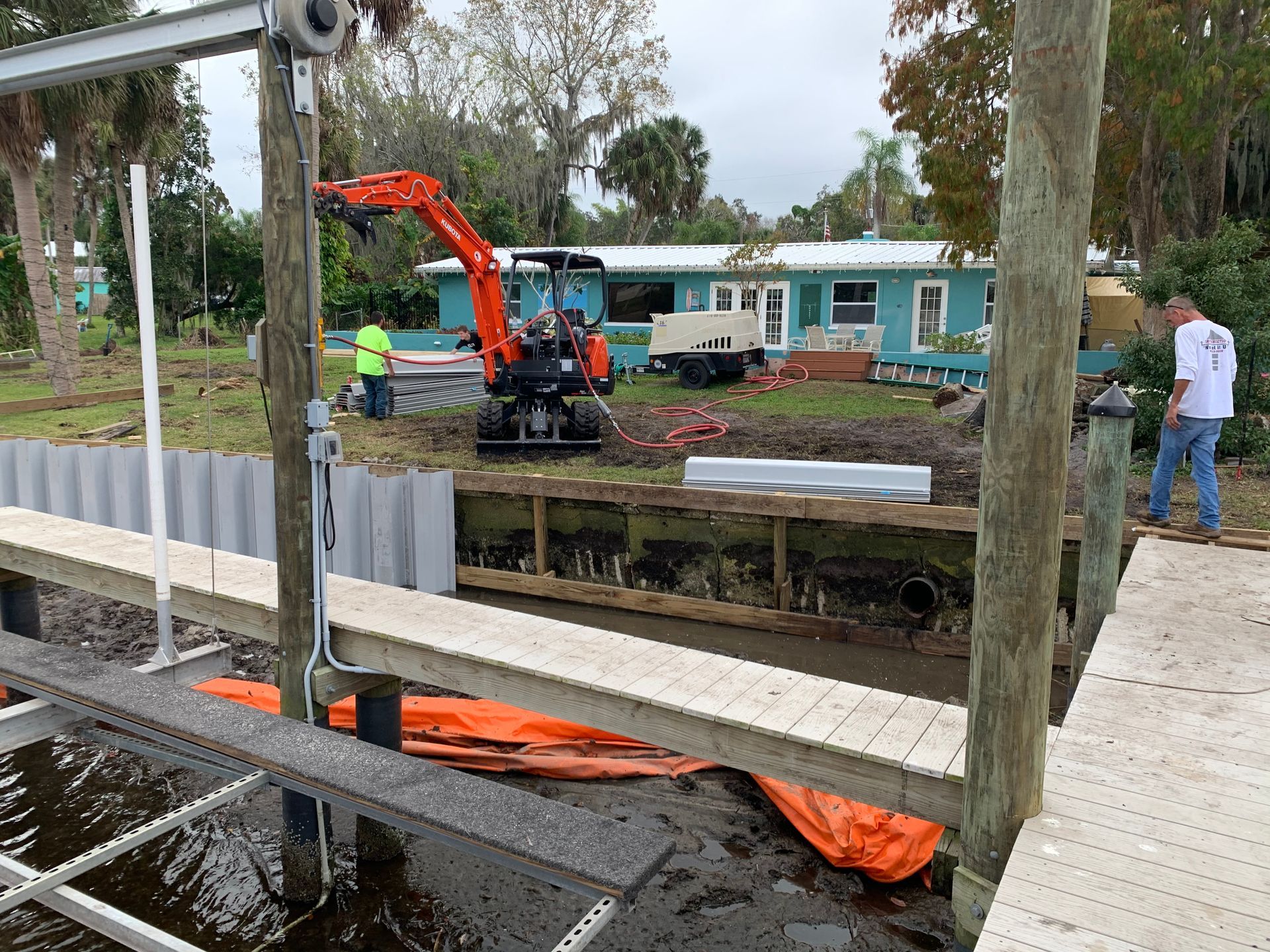 Construction site: excavator, dock, retaining wall. Men working on a waterfront property.