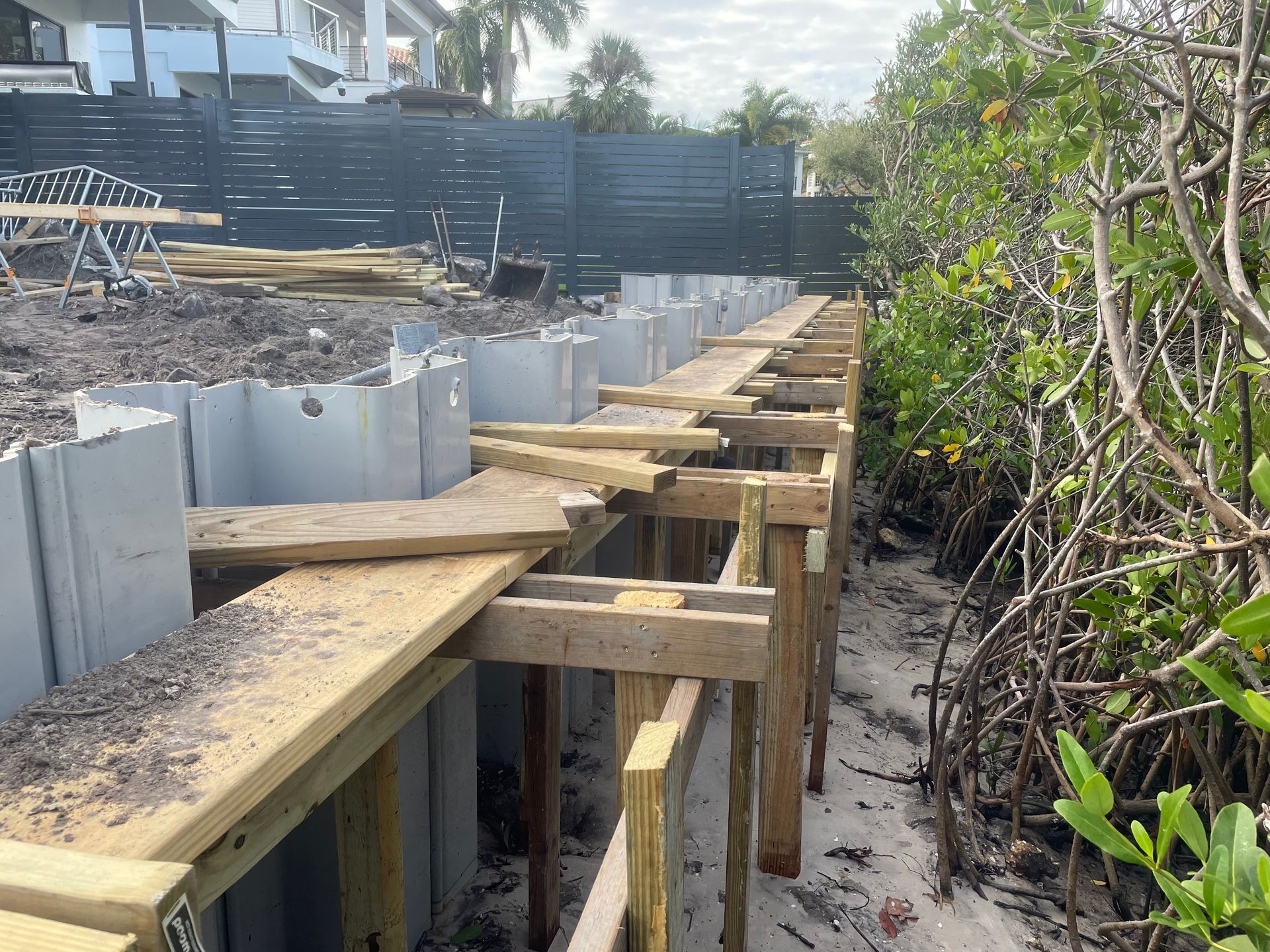 Construction site with a retaining wall being built on a beach, featuring metal and wooden materials.