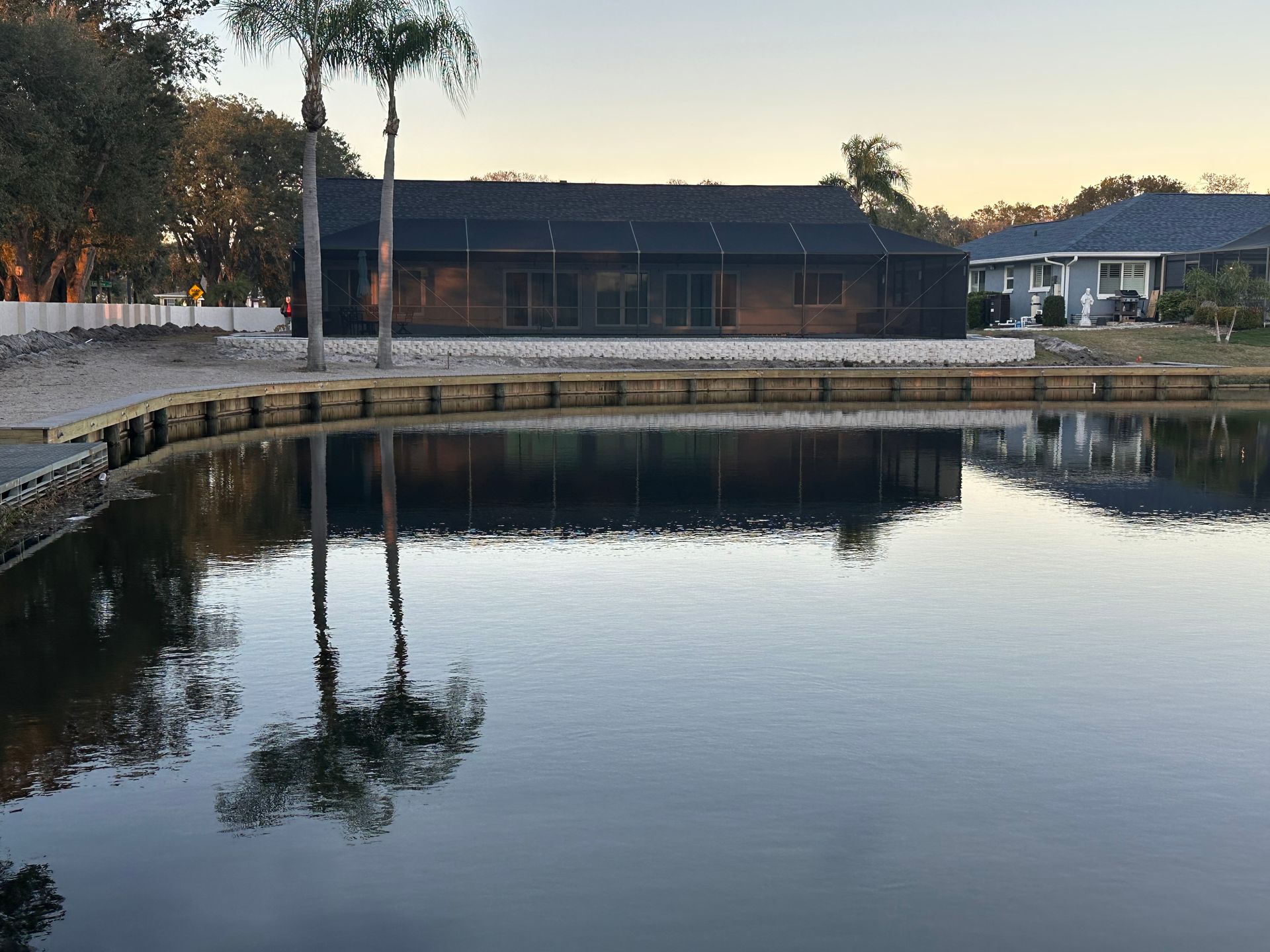 A serene pond reflects a house with a screened porch and a palm tree on a sunny day.