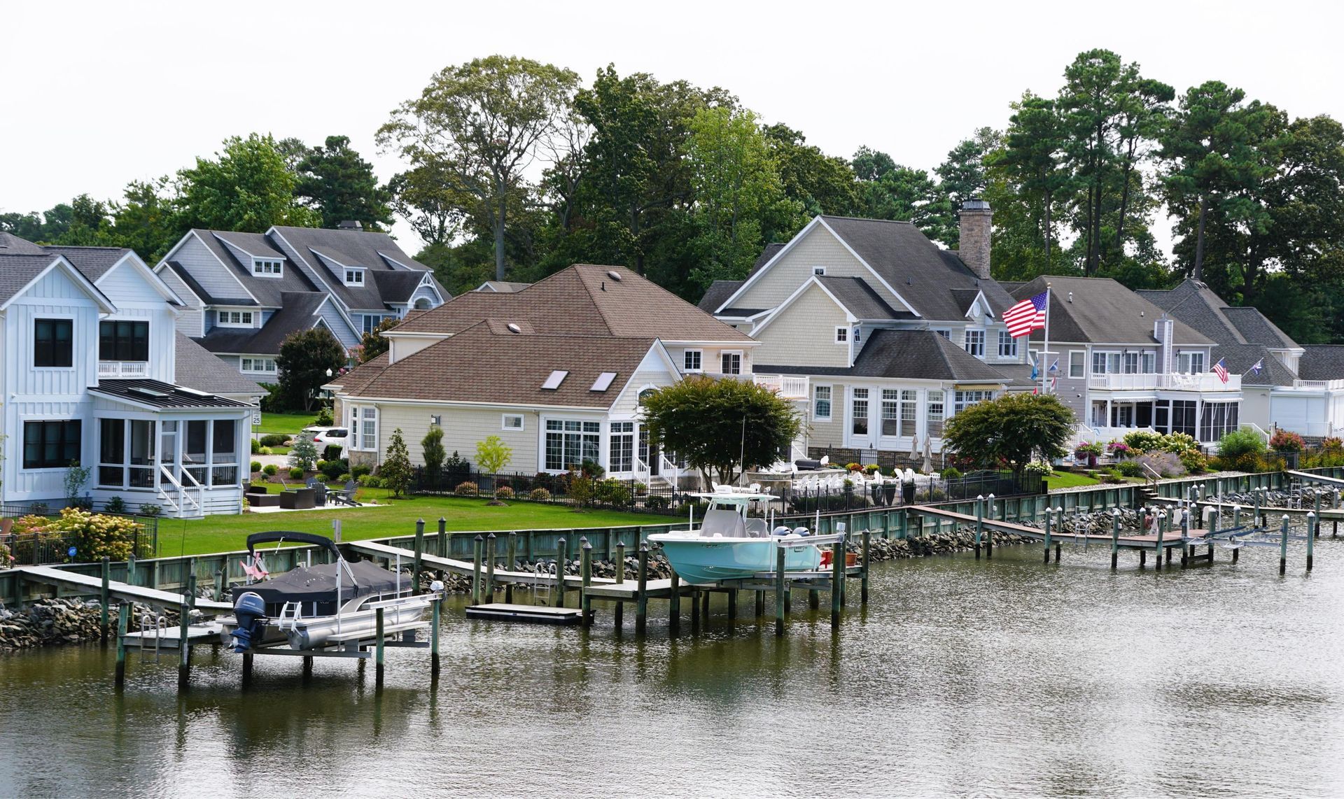 Waterfront homes with boat docks and boats, trees in the background.