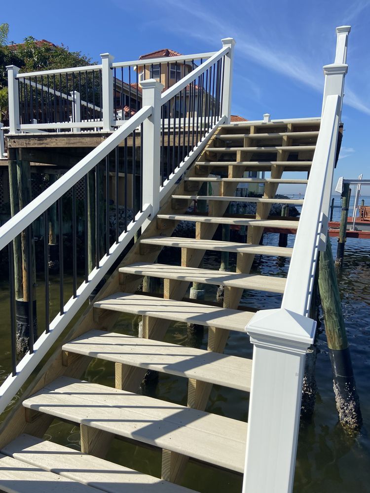 Wooden staircase leading down to water, white railings with black spindles, blue sky.