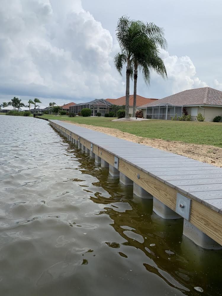 A wooden dock along a body of water in a residential area. Gray decking with water and houses in the background.