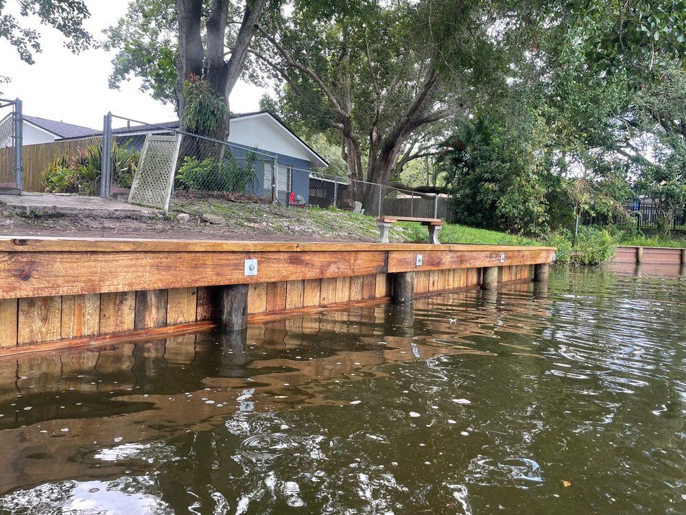 Wooden seawall on a body of water with a house in the background. Brown, green and tan colors.