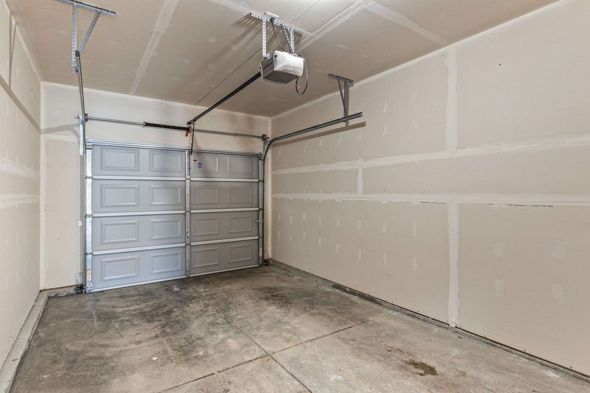 Empty unfinished garage with concrete floor, drywall walls, and a closed white garage door