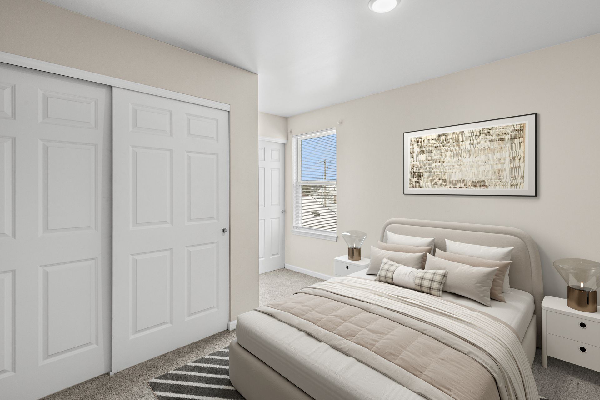 Bright modern bedroom with a bed, white closet doors, nightstand, and framed wall art.