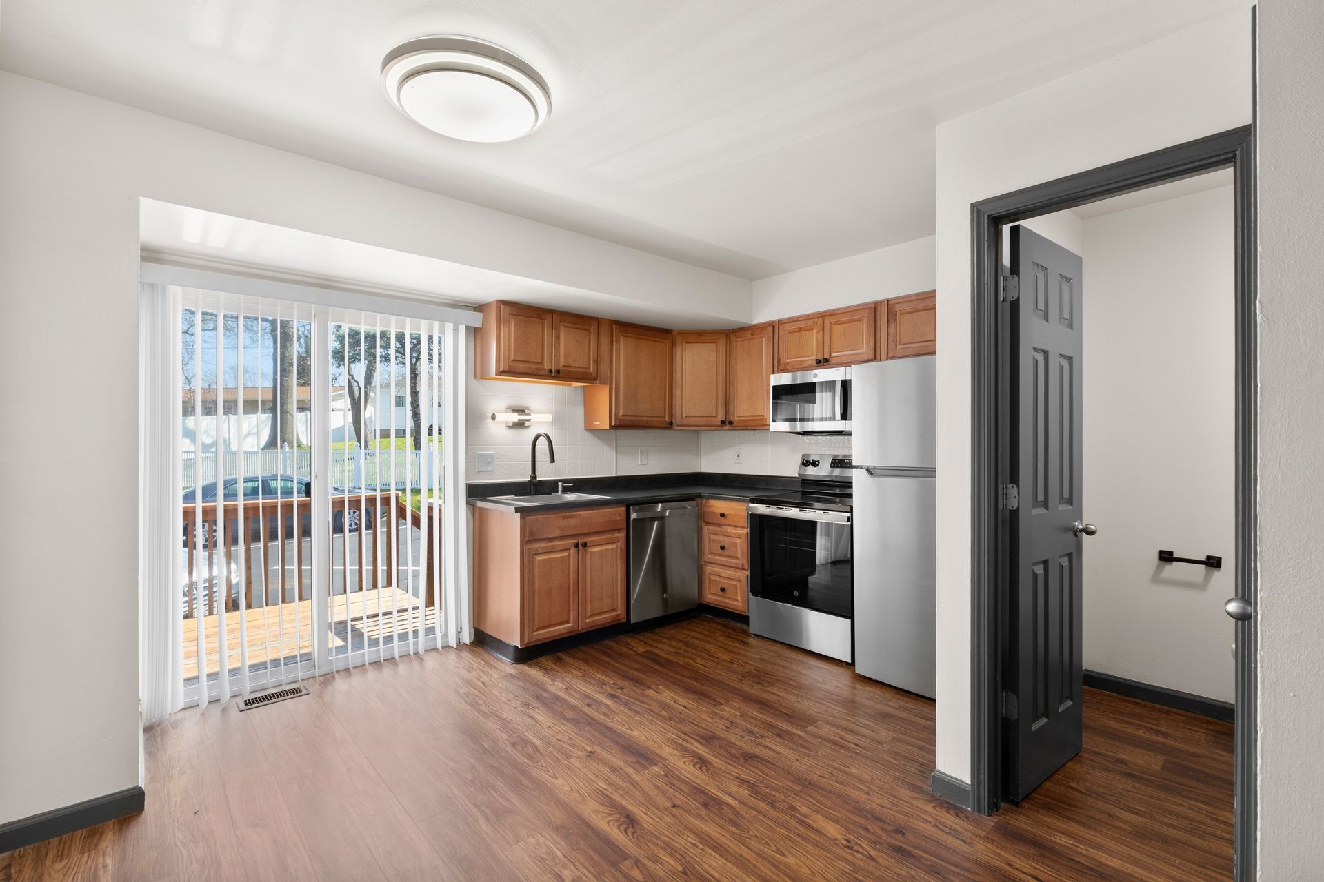 Empty kitchen with wood floors, white walls, oak cabinets, black appliances, and sliding glass doors.