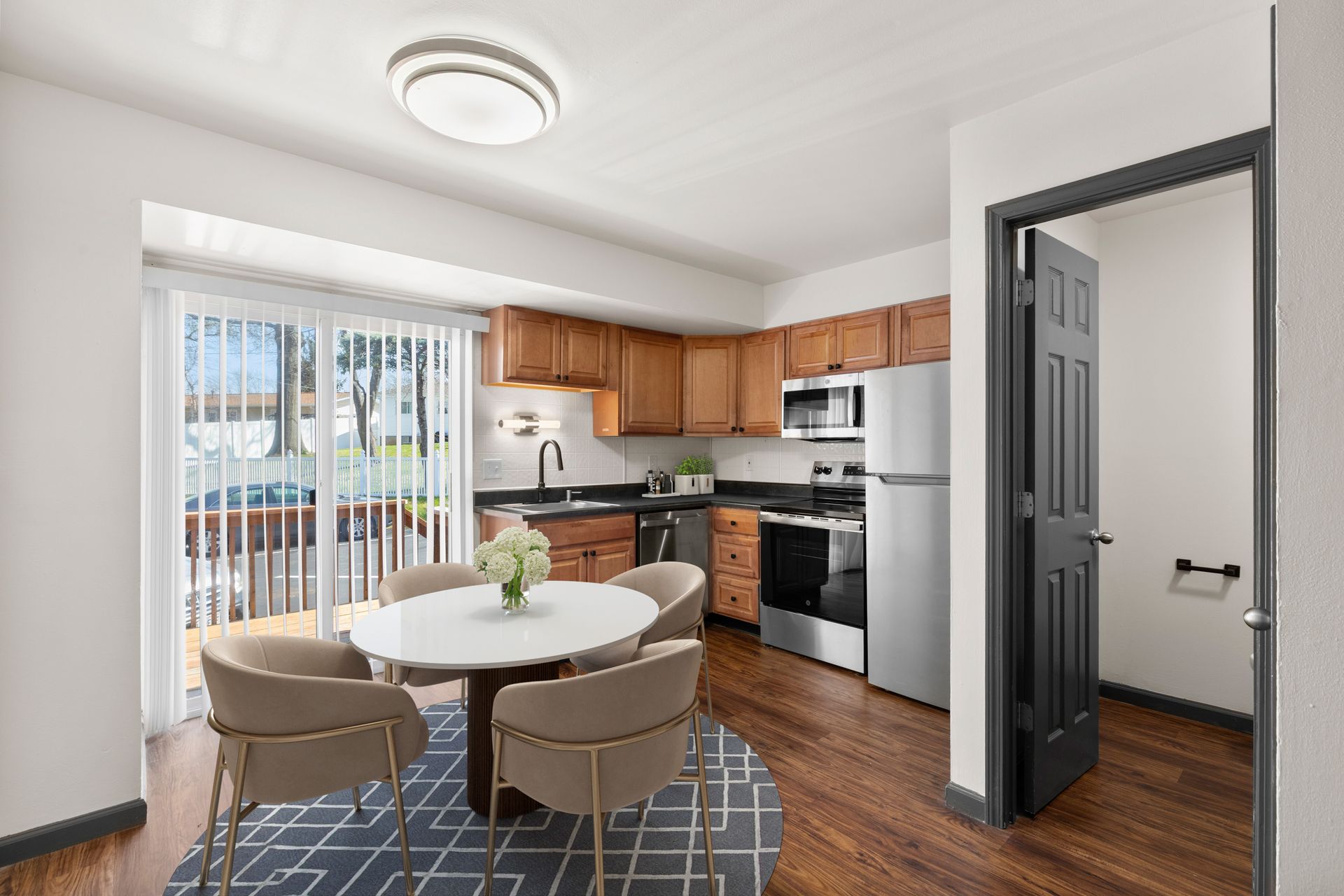 Bright kitchen with round dining table, wooden cabinets, black appliances, and sliding glass door.
