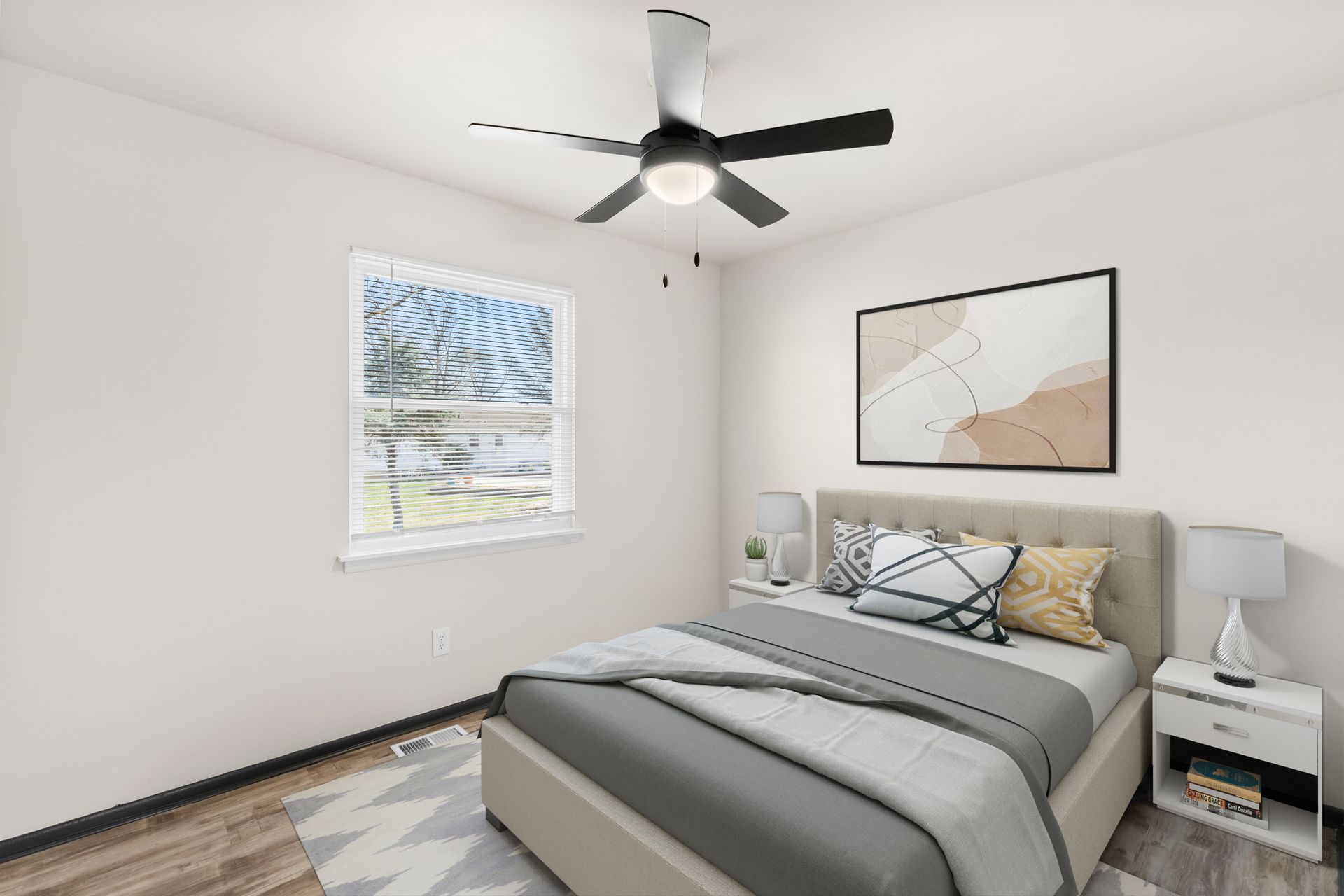 Modern bedroom with gray bed, ceiling fan, two windows, and framed wall art.