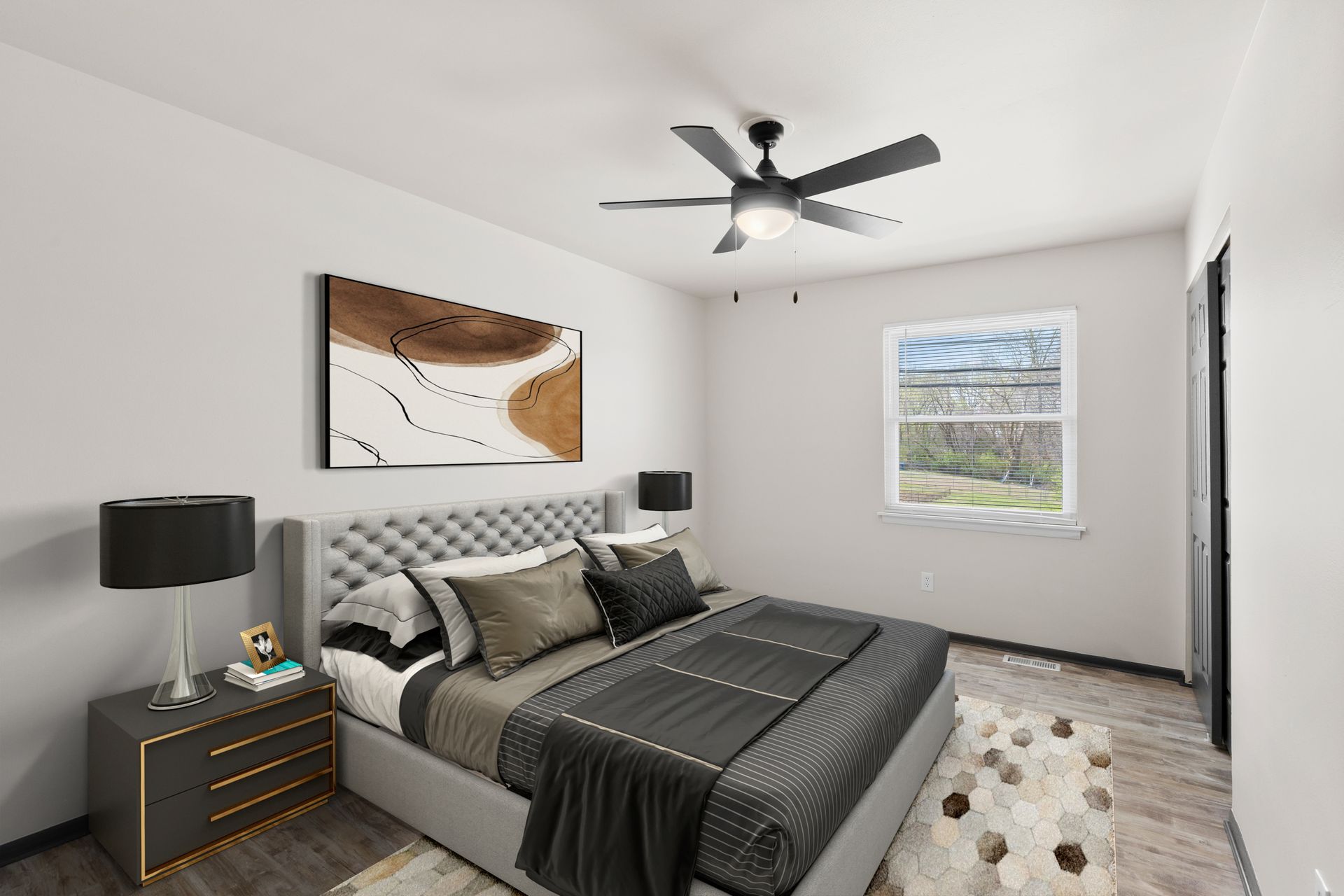 Modern bedroom with gray bed, black accents, ceiling fan, nightstand, wall art, and window.