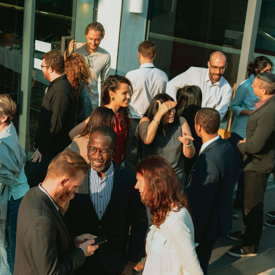 Crowd of people mingling outside a glass building, chatting in formal attire.