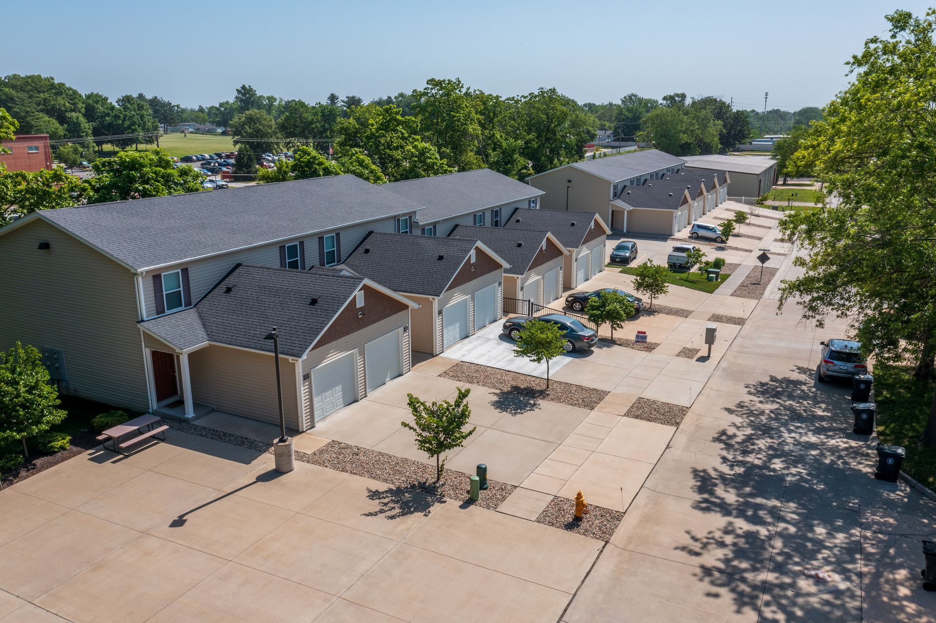 Aerial view of a townhouse complex with garages, a paved courtyard, and trees lining the street.