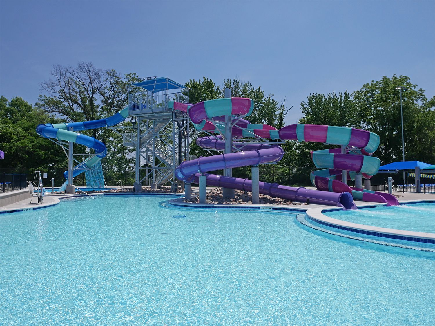 Water park pool with colorful blue, purple, and teal slides under a clear sky