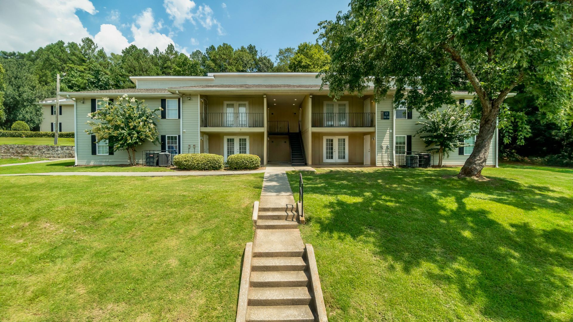 Large two-story house with a front lawn, central stairway, and trees under a blue sky