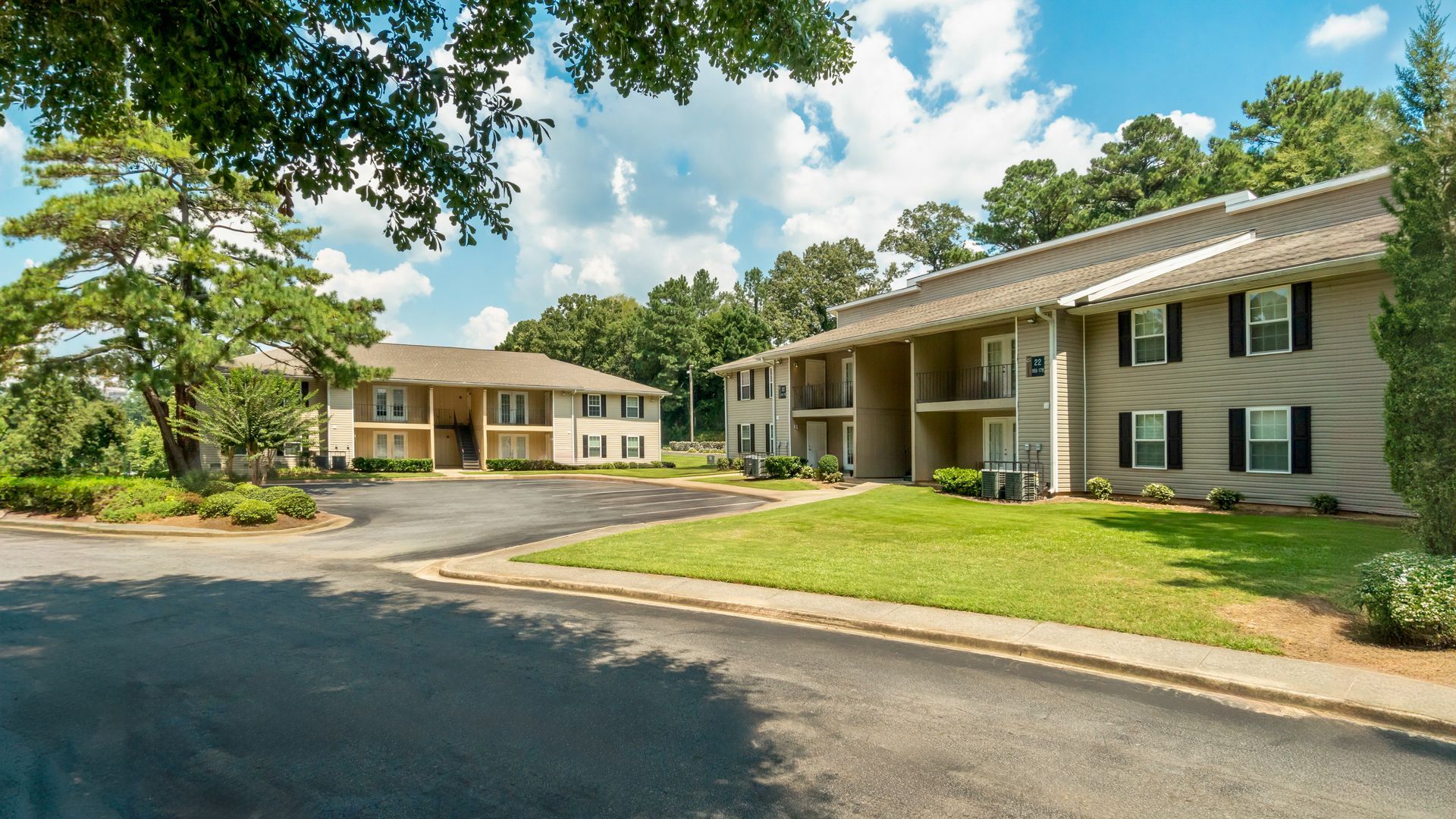 Apartment buildings and parking lot on a sunny day, with trees and blue sky