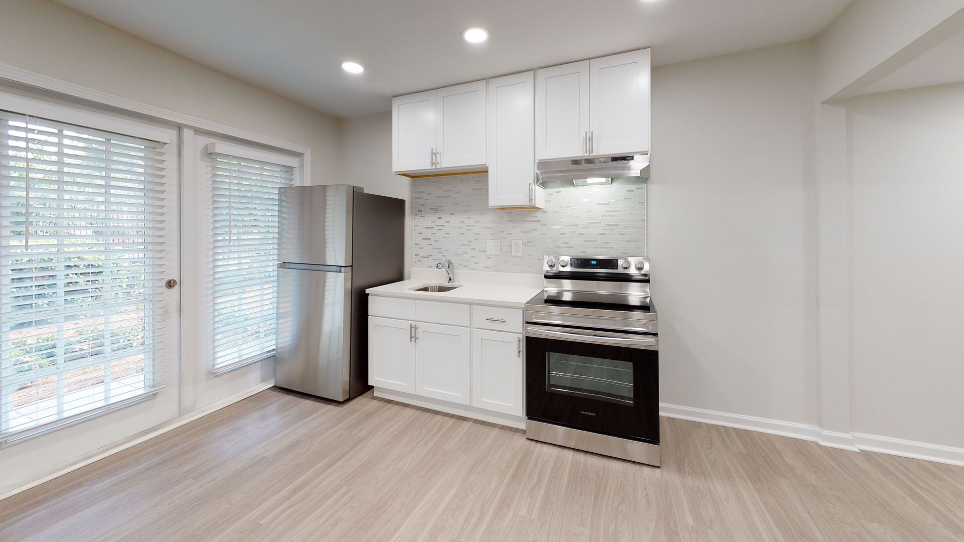 Bright modern kitchen with white cabinets, stainless steel appliances, and window blinds.
