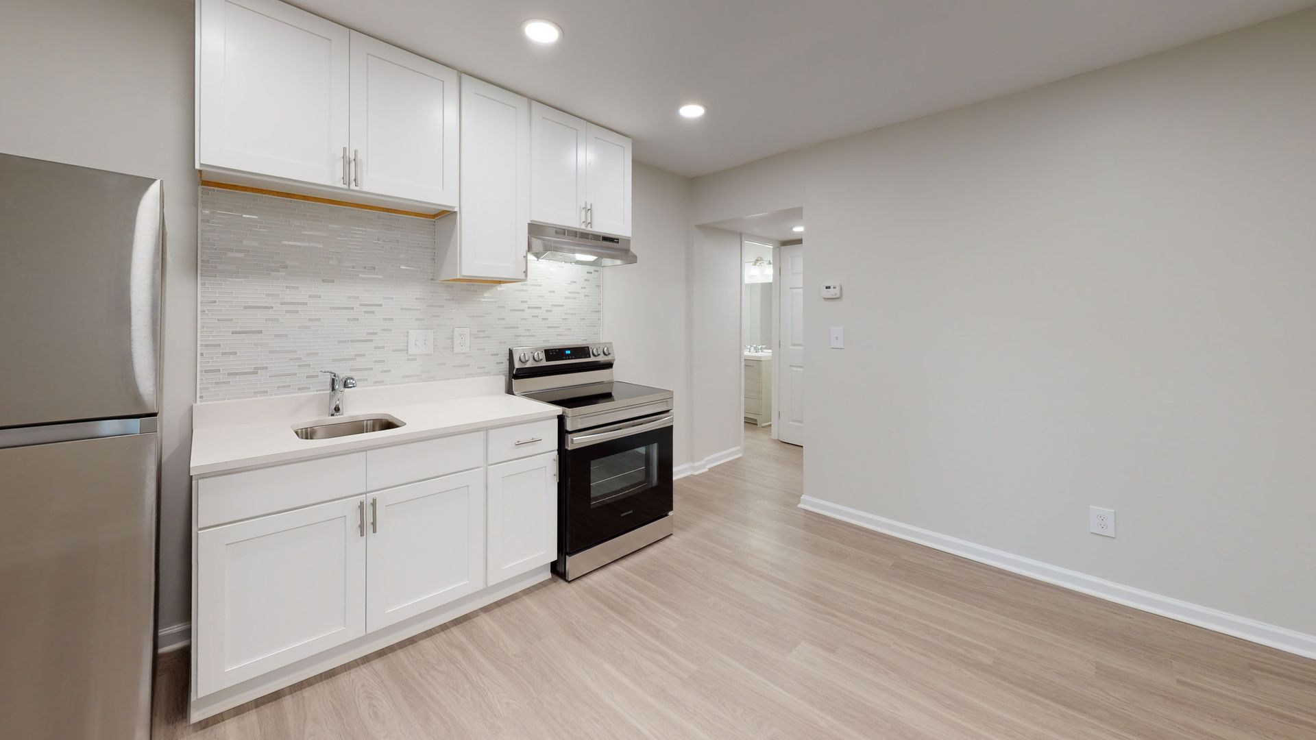 Empty modern kitchen with white cabinets, gray countertops, black fridge, and wood-look flooring