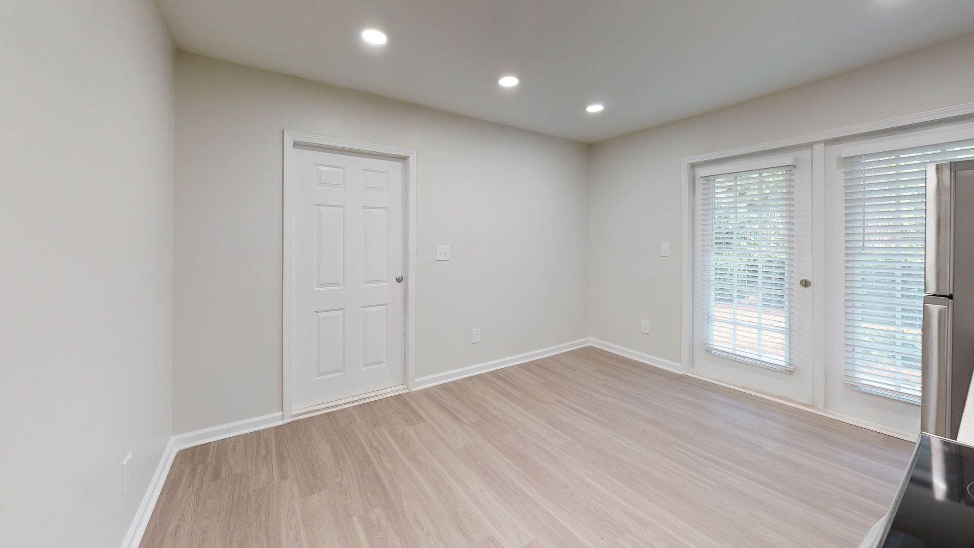 Empty bright room with light wood floors, white walls, recessed lights, and French doors to a balcony.