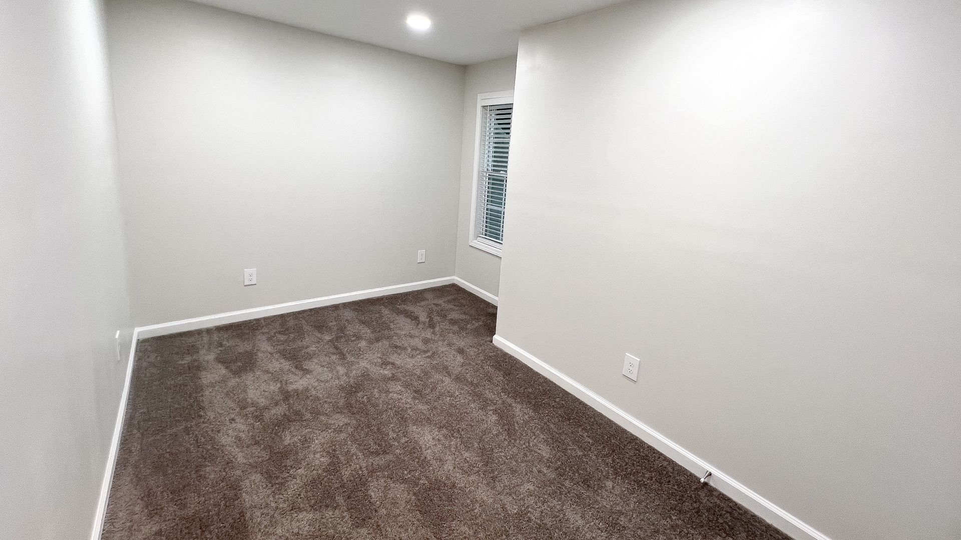 Empty carpeted room with white walls and a small window
