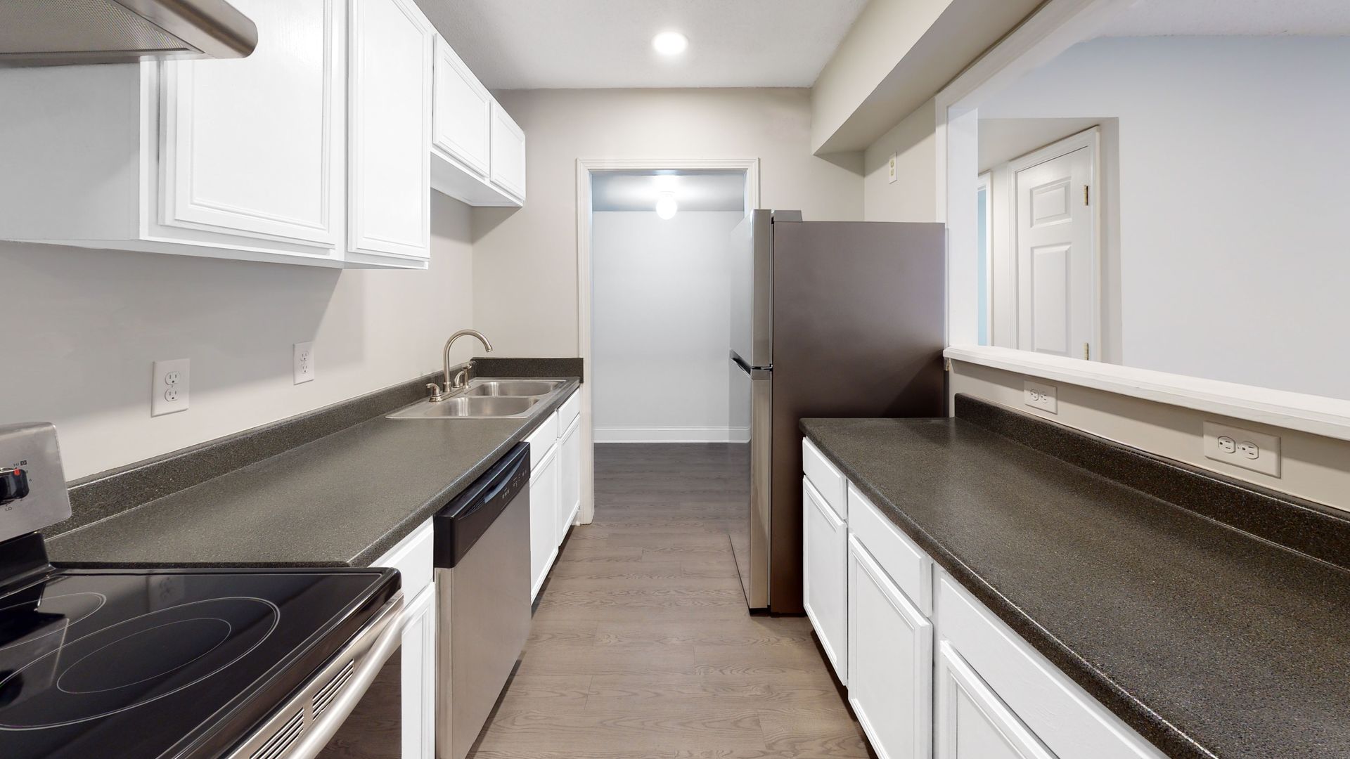Bright white galley kitchen with dark countertops, white cabinets, and a stainless refrigerator end view