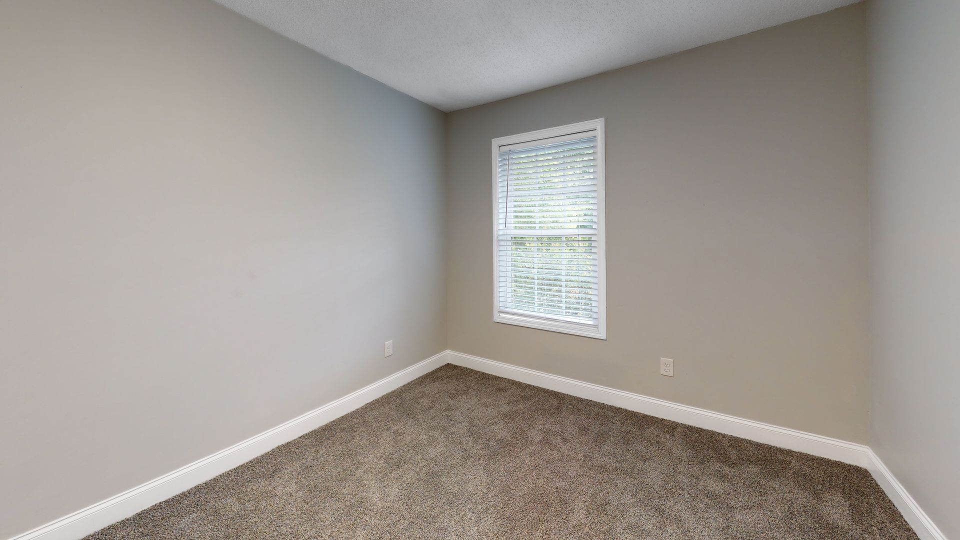 Empty beige bedroom corner with carpet and a small window with blinds