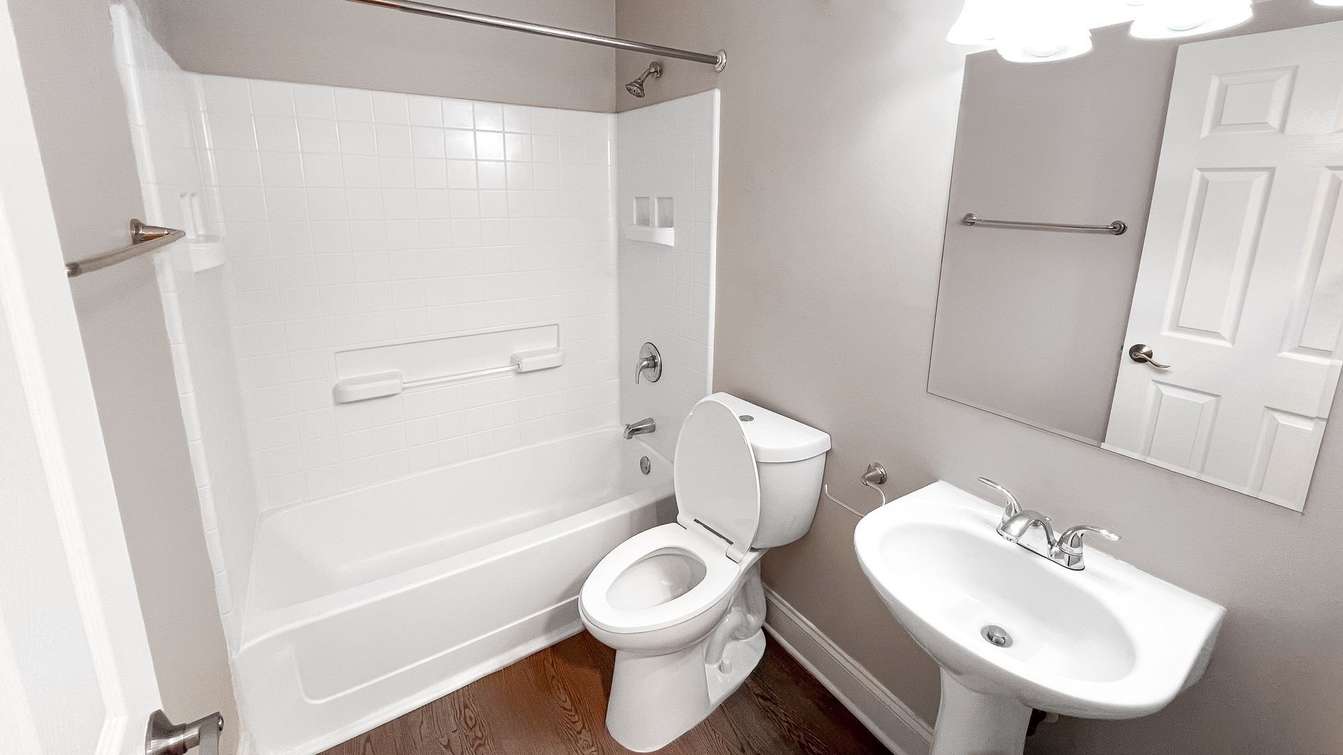 Bright white bathroom with tub, toilet, pedestal sink, and large mirror.