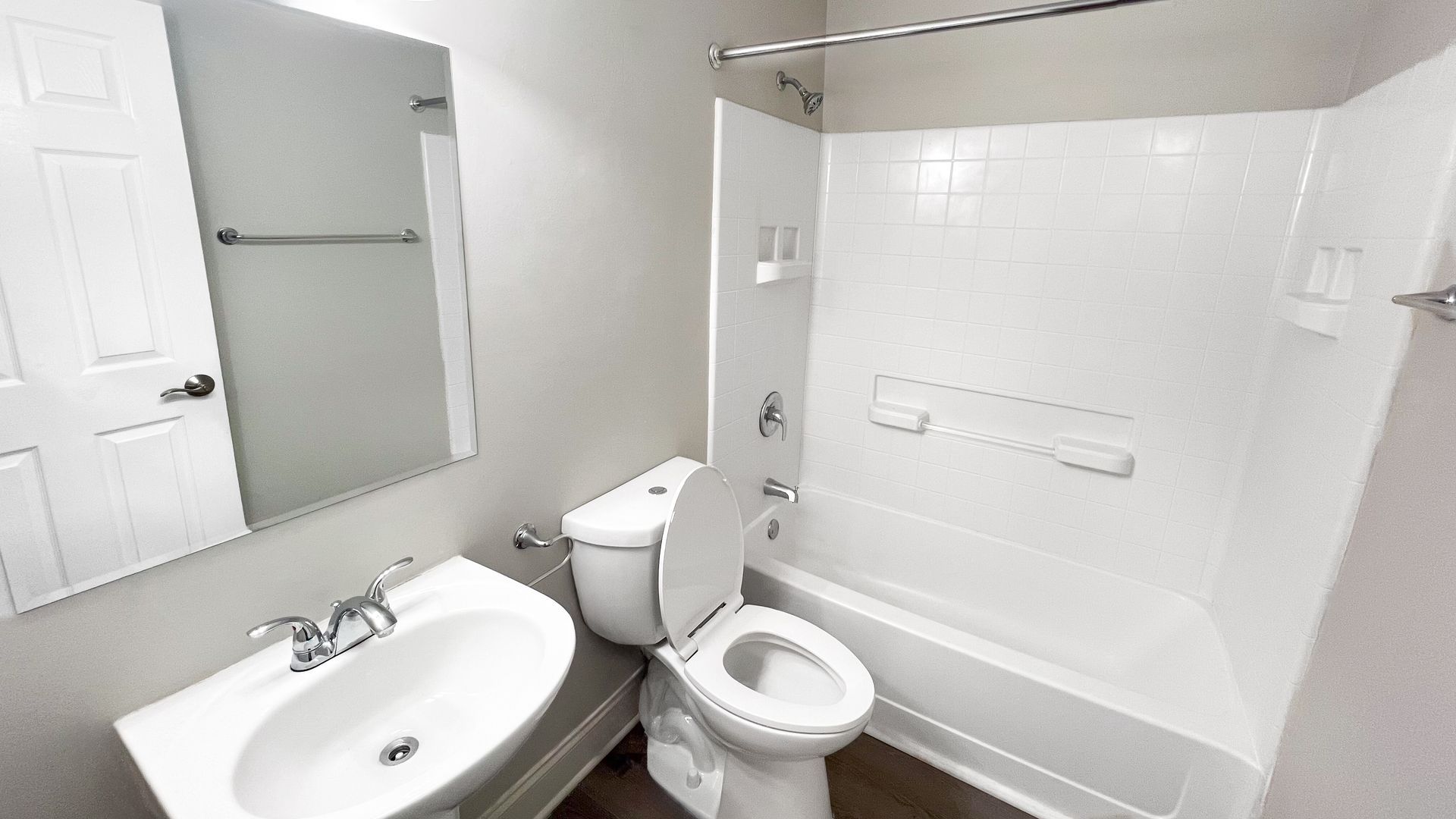 Small white bathroom with sink, mirror, toilet, and bathtub with tiled shower surround