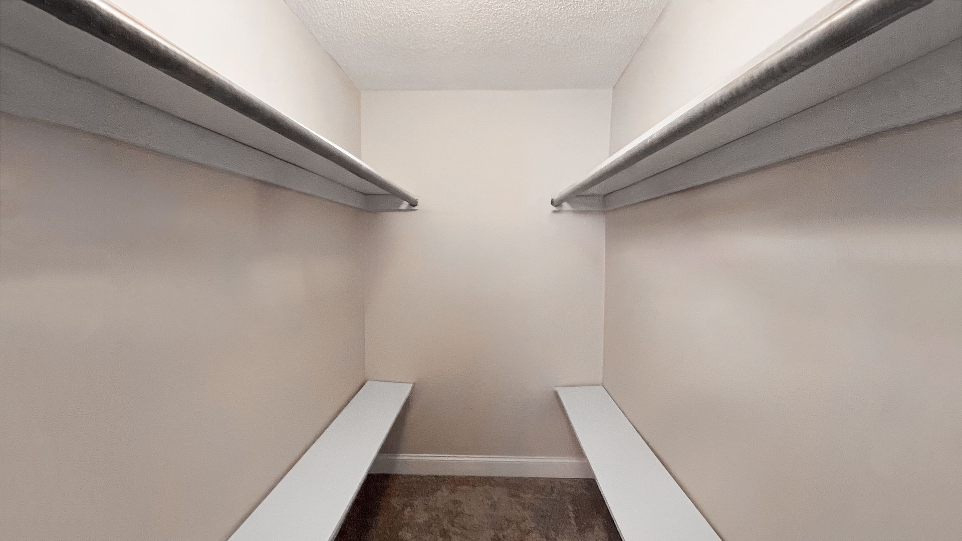 Empty walk-in closet with white shelves and hanging rods on both sides.