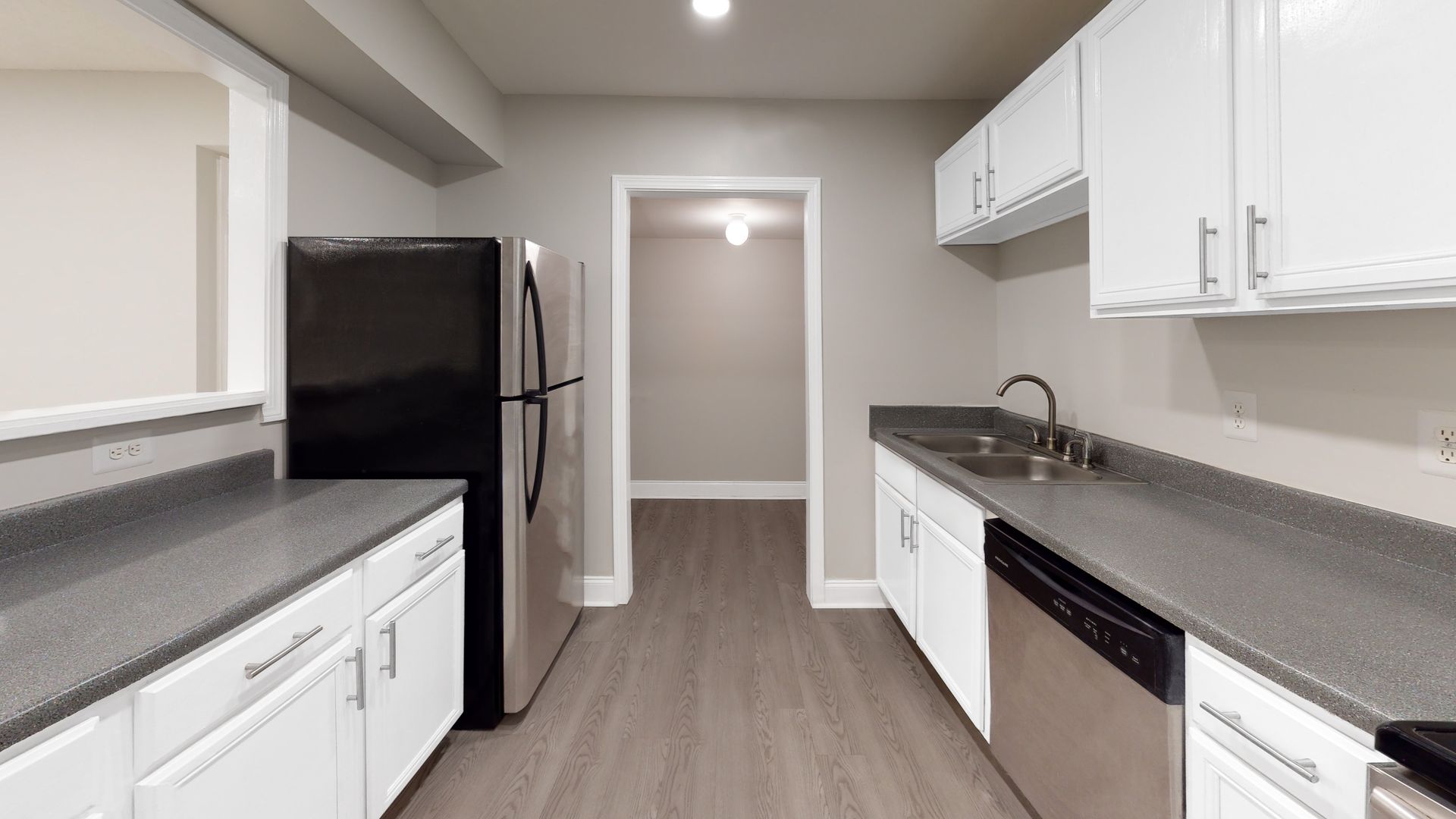 Bright kitchen with white cabinets, gray countertops, black appliances, and wood-look flooring.