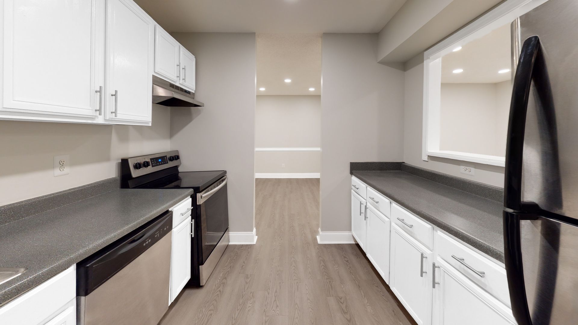 Bright modern galley kitchen with white cabinets, gray counters, stainless appliances, and wood-look floors