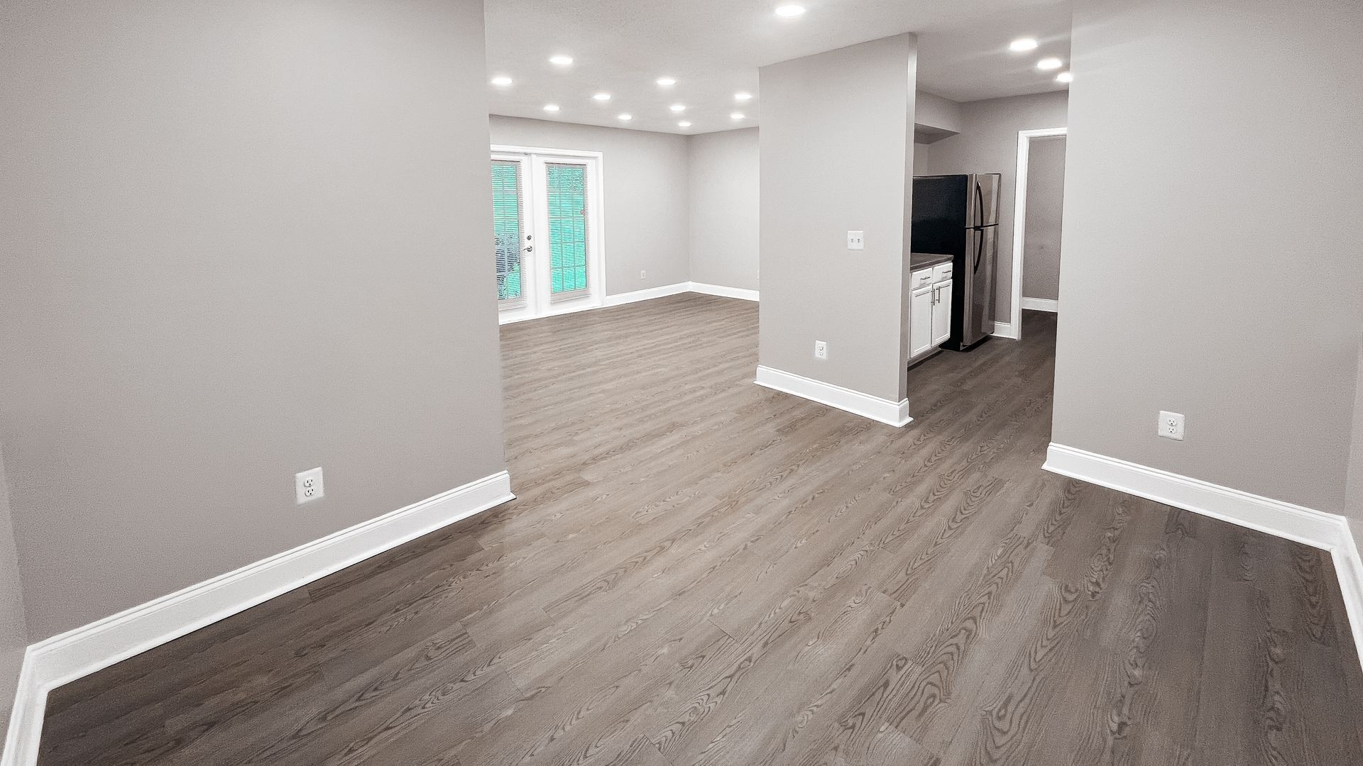 Empty modern living room with gray walls, wood-look floors, and bright recessed lighting