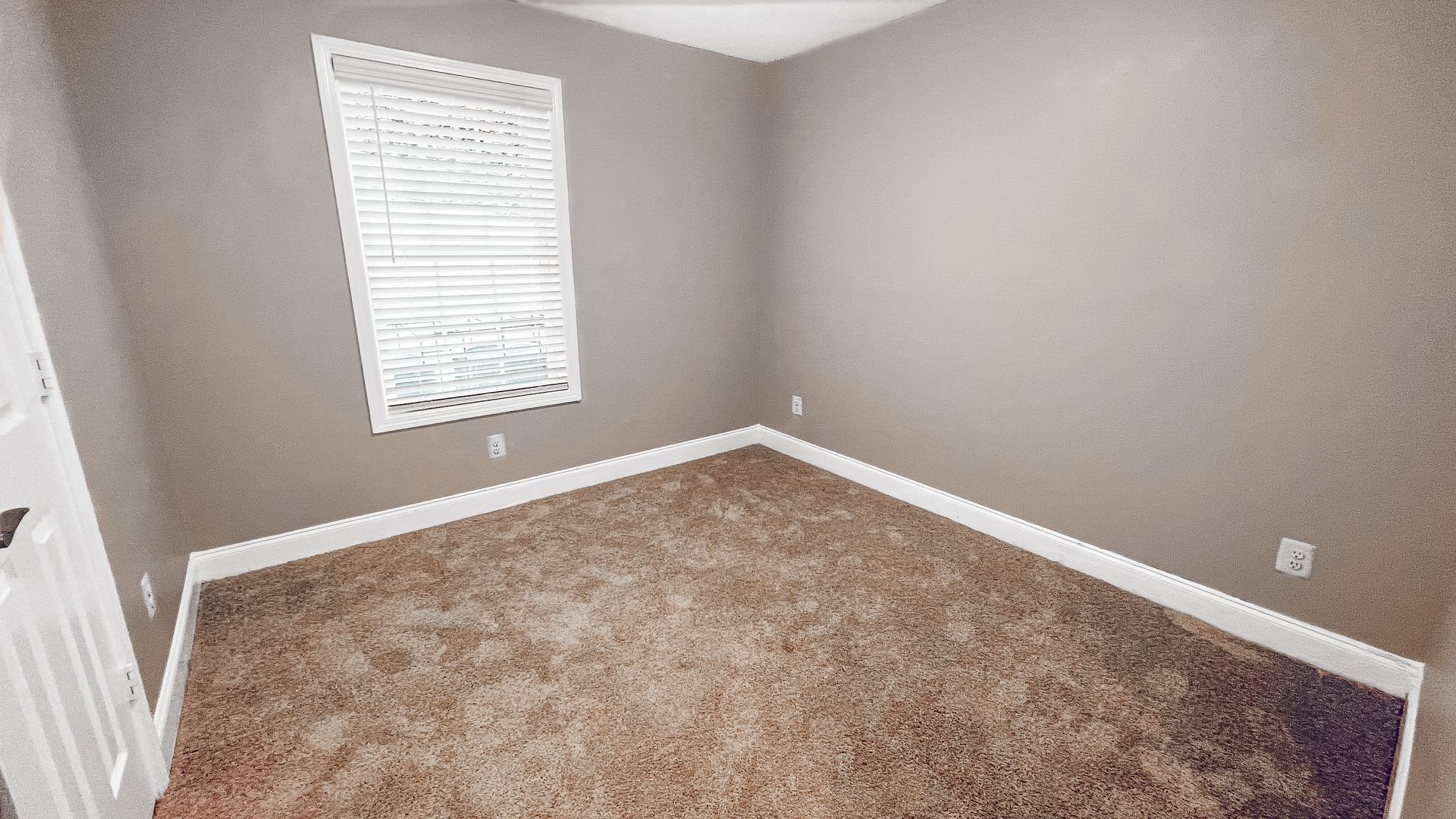Empty beige bedroom with tan carpet, white trim, and a window with blinds.