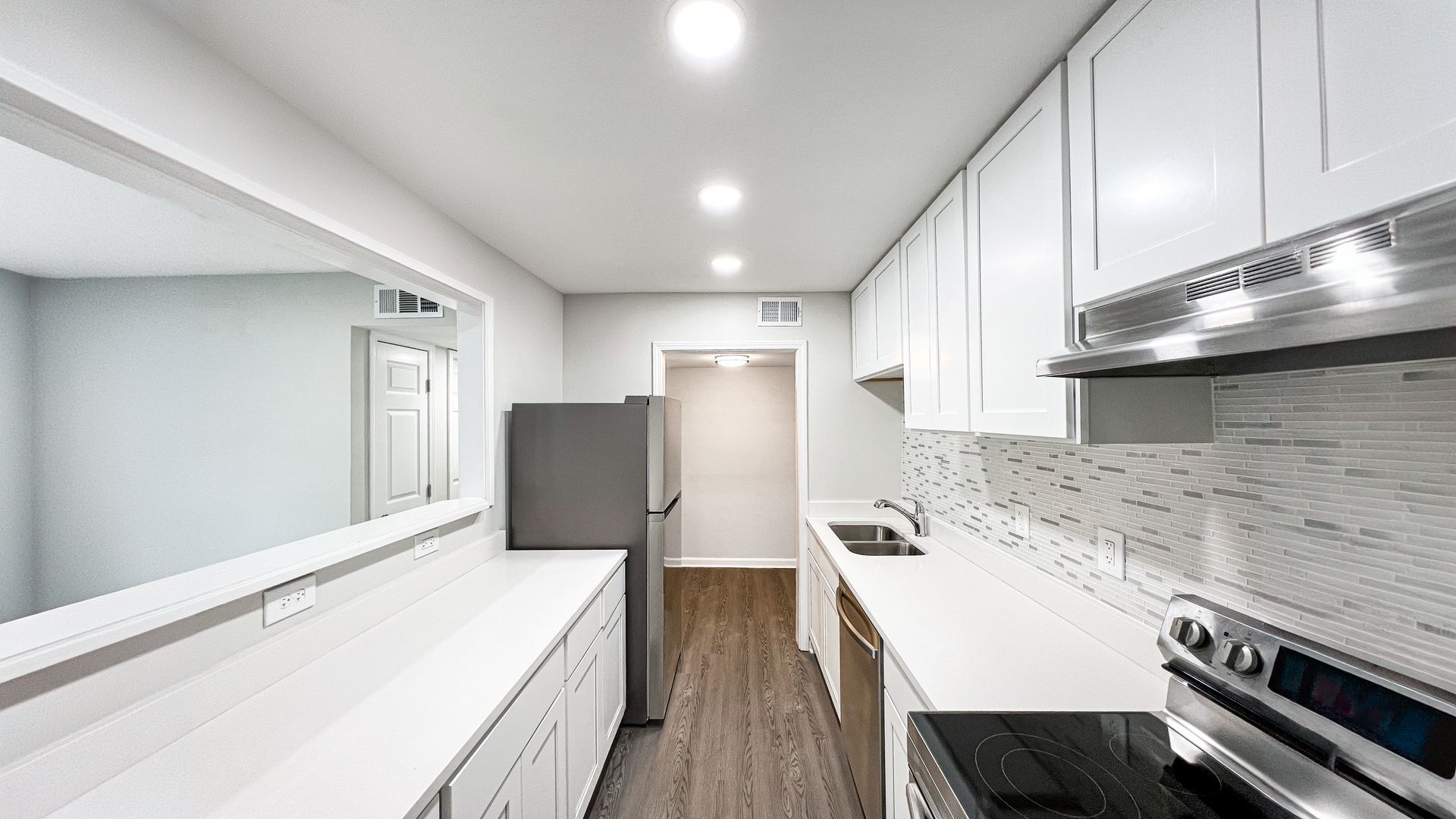 Bright white galley kitchen with long counter, stainless stove, and wood flooring