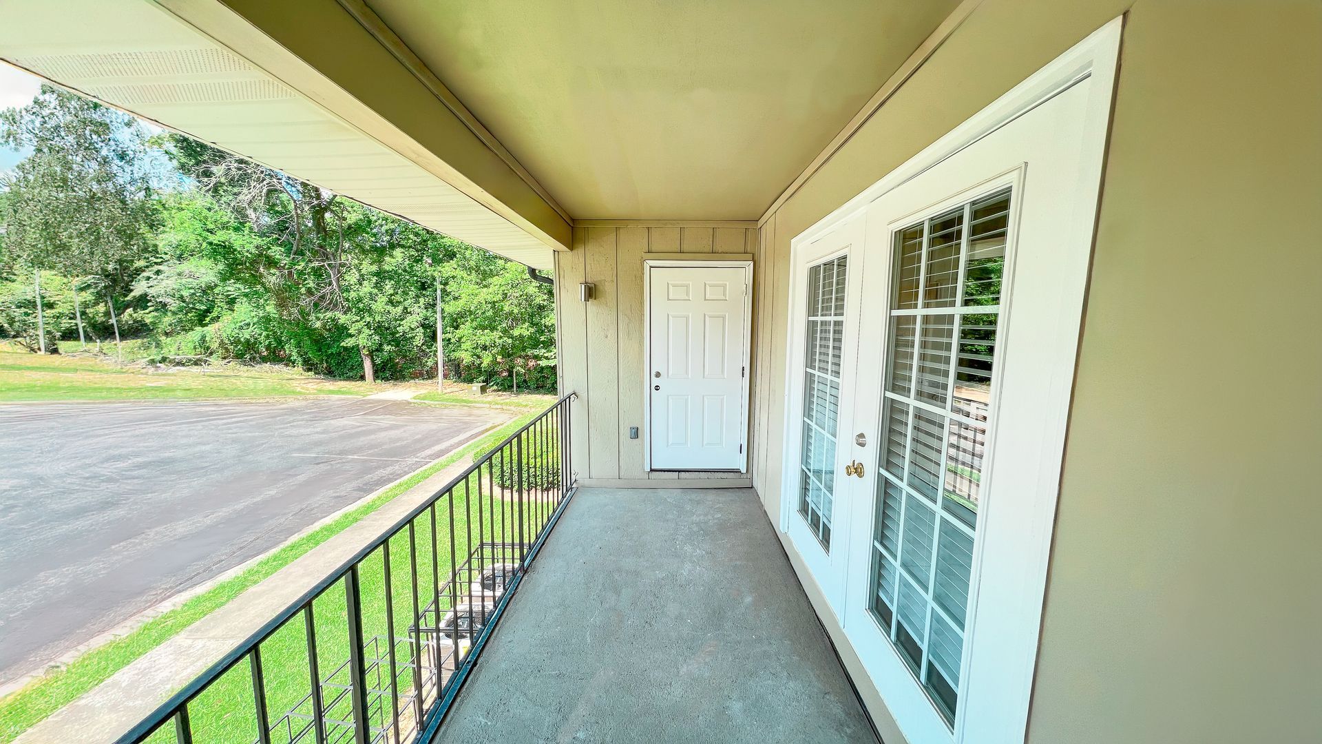 Covered apartment porch with railing, white door and French doors, overlooking a tree-lined street.