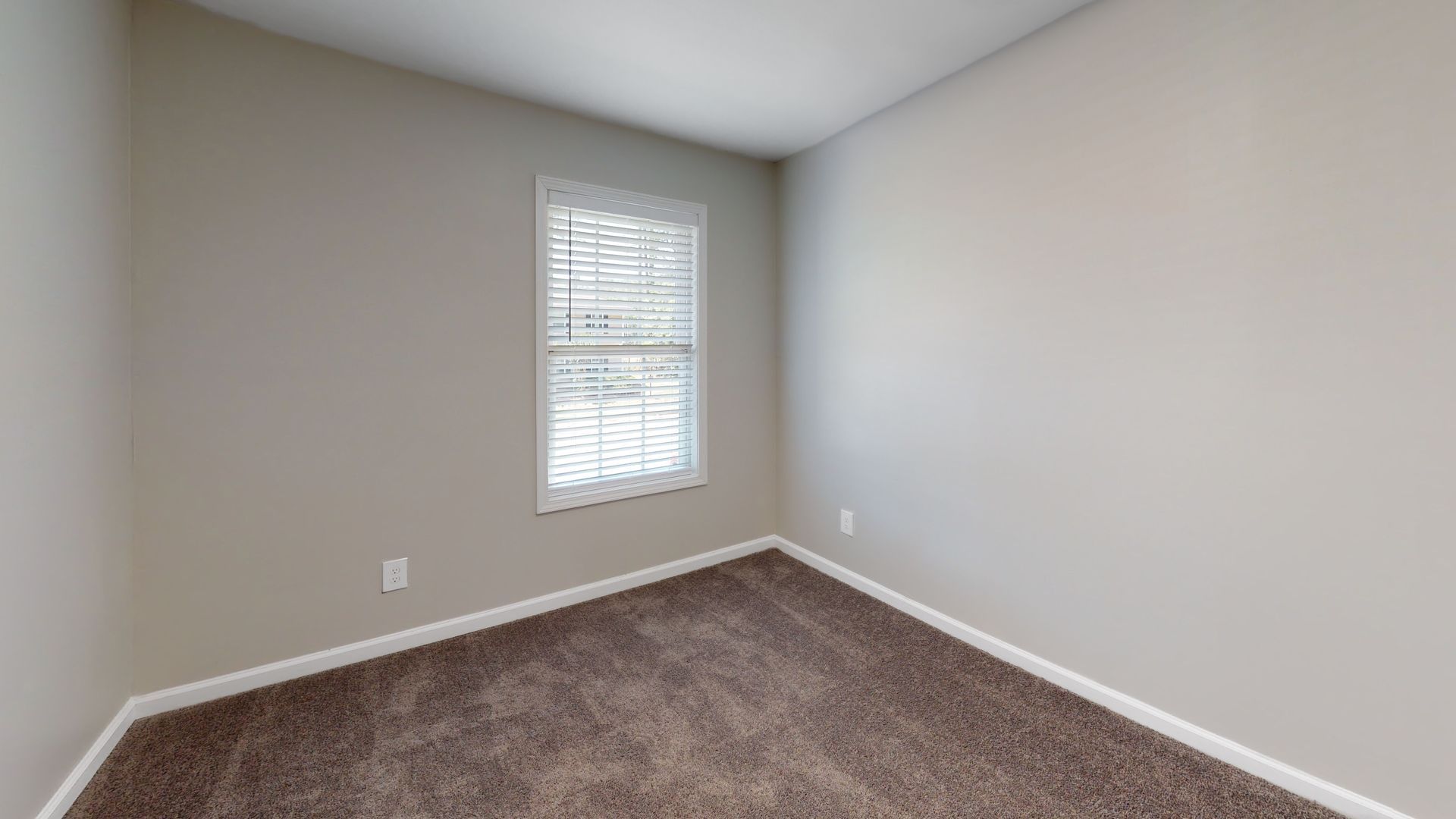 Empty beige bedroom with carpet and a small window with blinds.