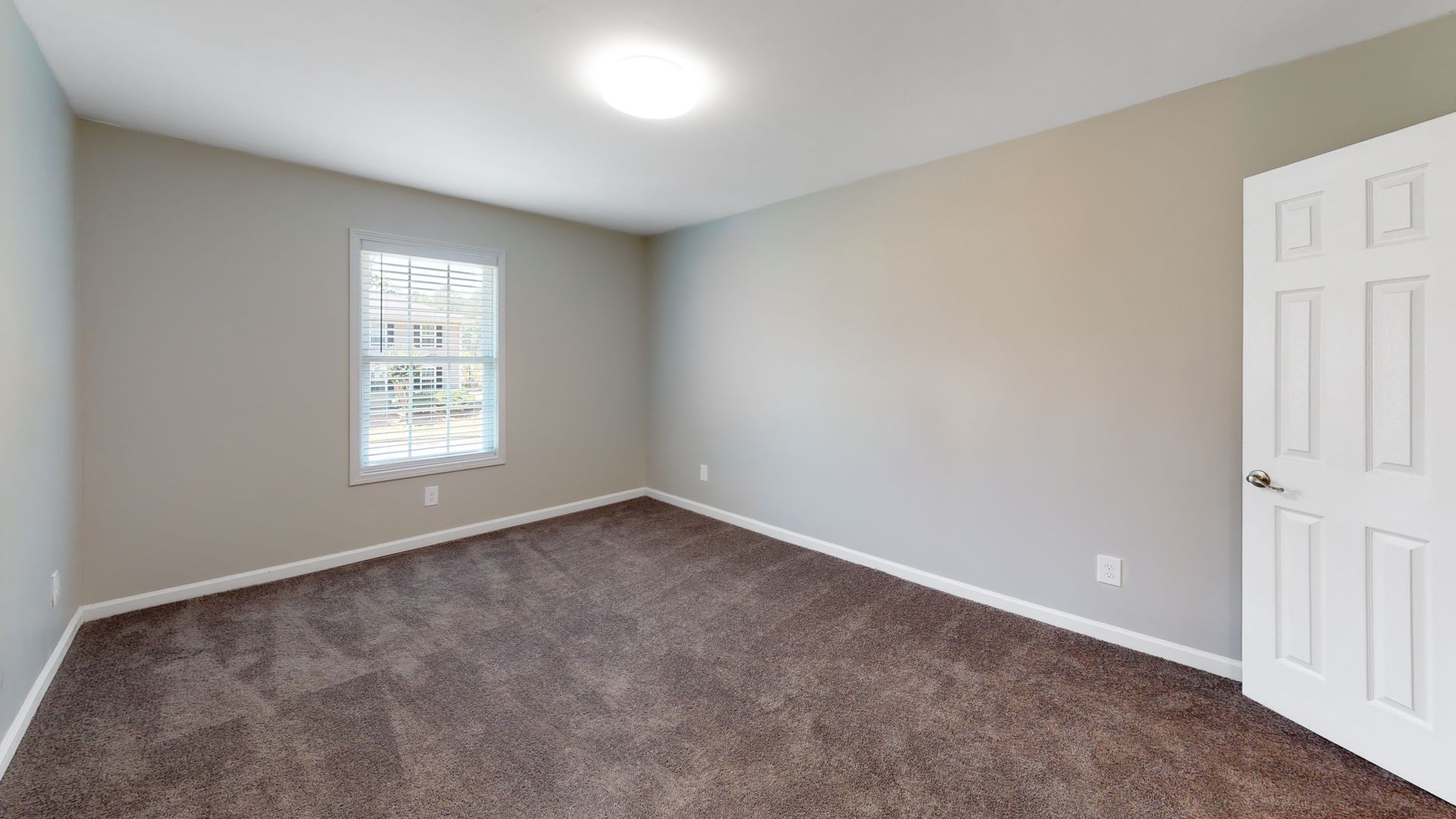 Empty beige bedroom with gray carpet, white trim, a window, and an open closet door.