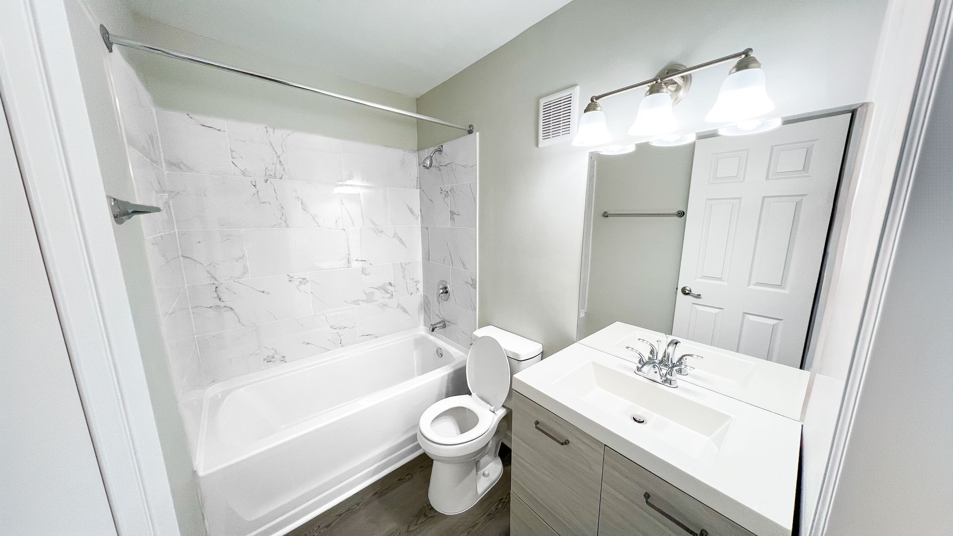 Bright white bathroom with tub-shower, toilet, and vanity with mirror and lights