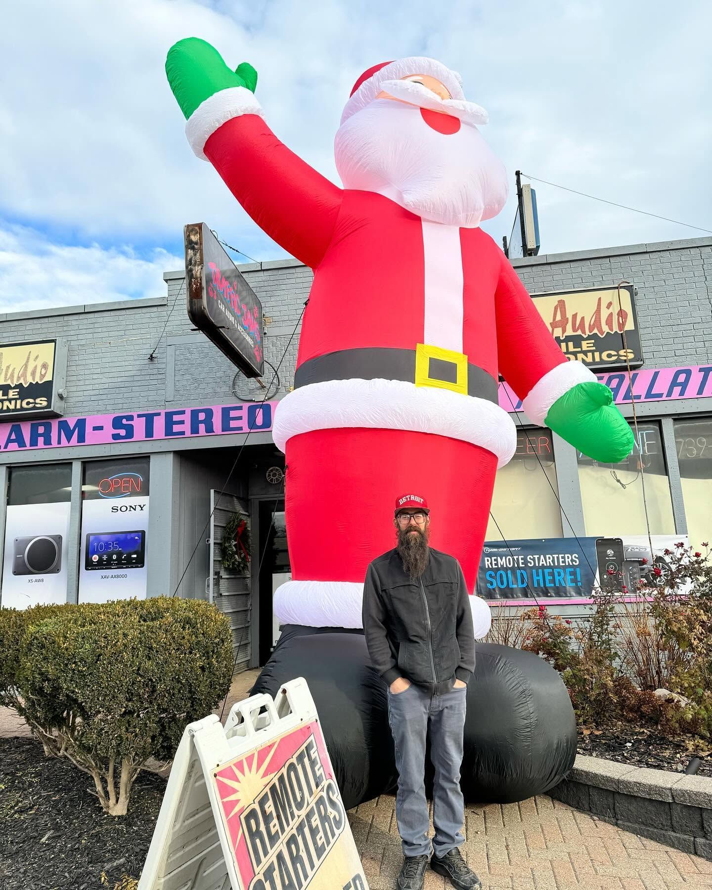 Man posing beside a giant inflatable Santa in front of a store