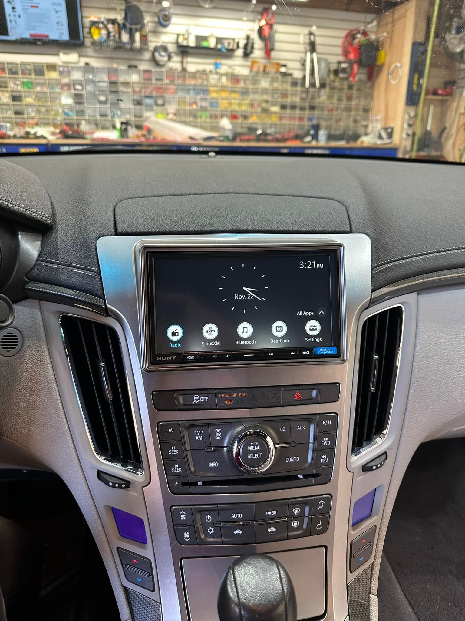 Car dashboard with a touchscreen infotainment system and climate controls, parked inside a shop or garage.