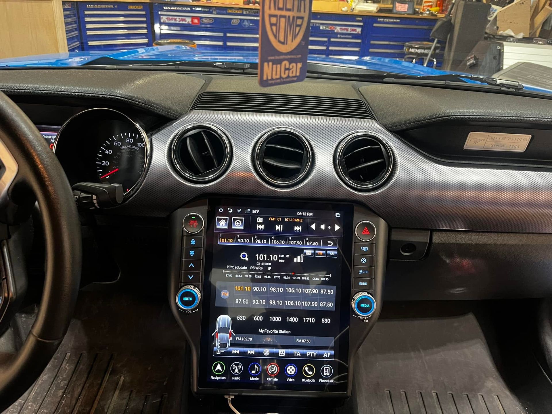 Car dashboard with a large vertical touchscreen showing a music app, viewed from the driver’s seat.