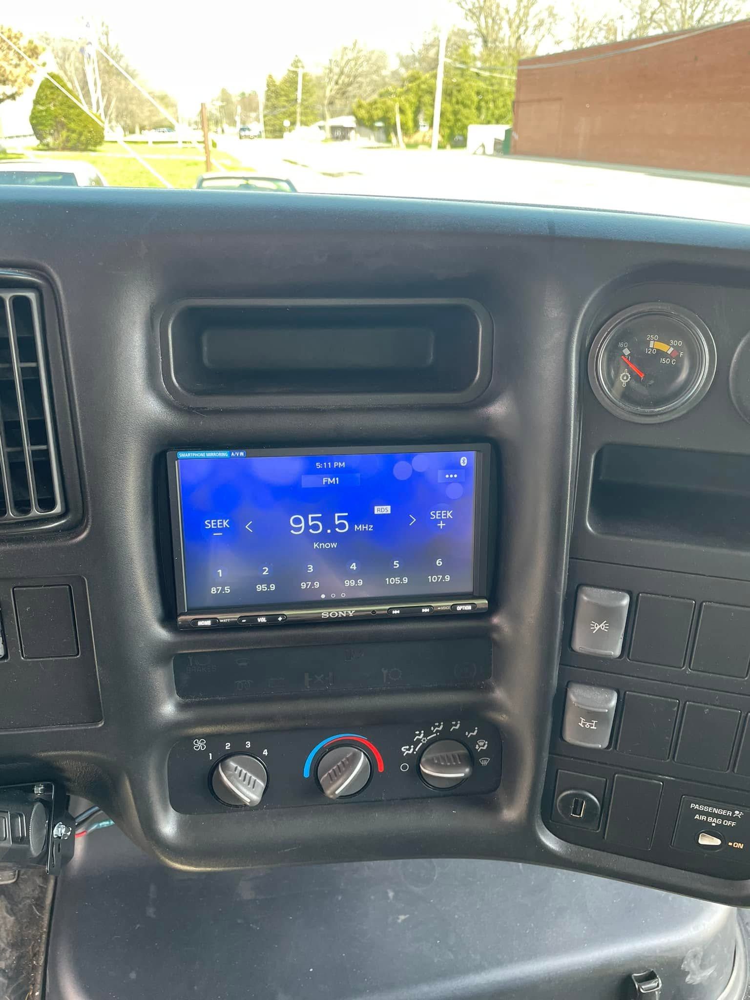 Car dashboard with a blue-lit stereo display, vents, knobs, and gauges in a parked vehicle.