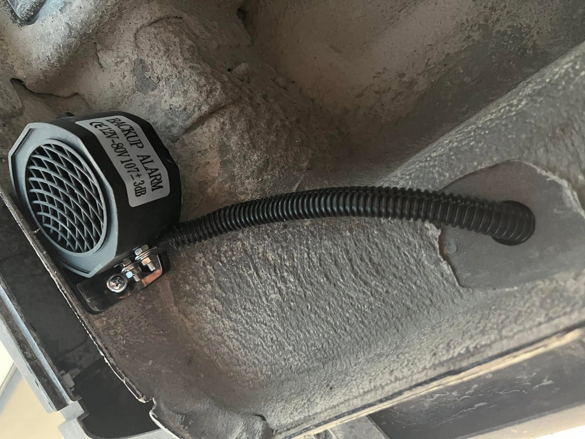 Small black speaker or siren unit with a corrugated hose mounted on a gray textured surface.