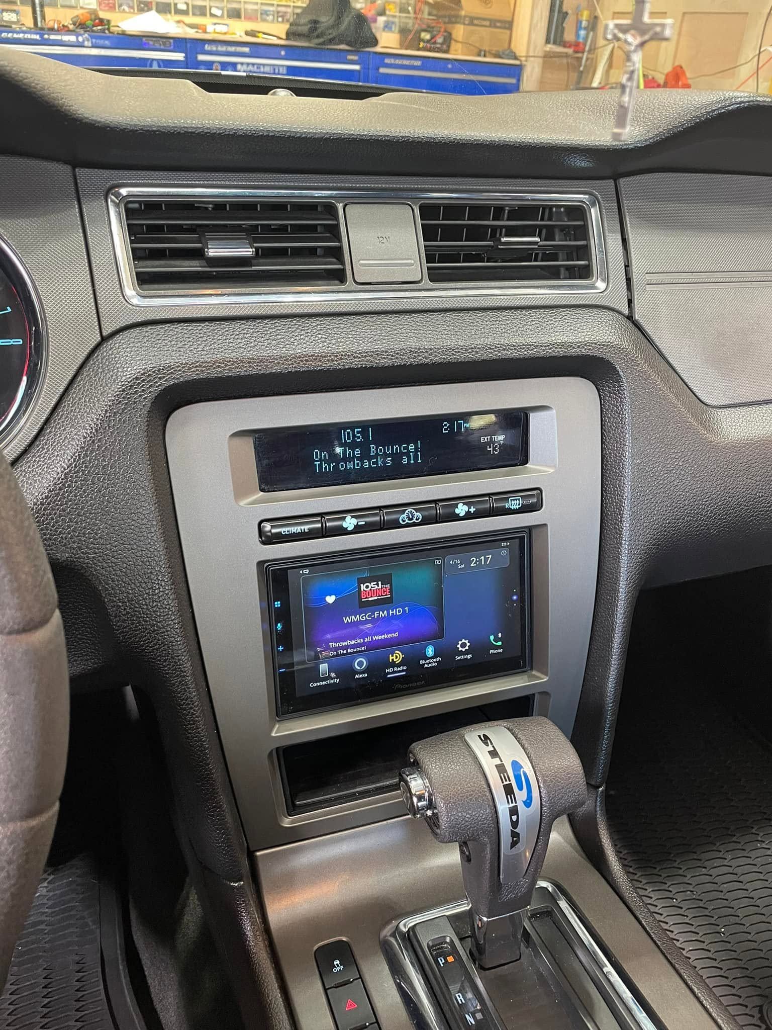 Car dashboard with center air vents, infotainment screen, and automatic gear shifter in a textured gray interior
