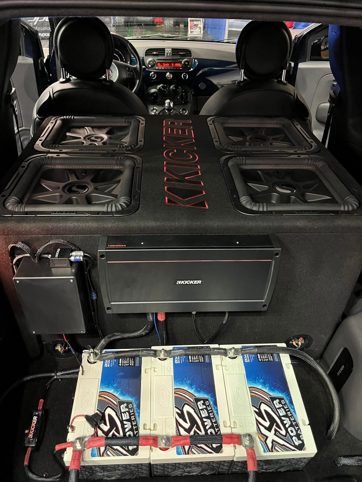Car trunk with a custom audio setup, speakers and amplifiers mounted throughout the cargo area.