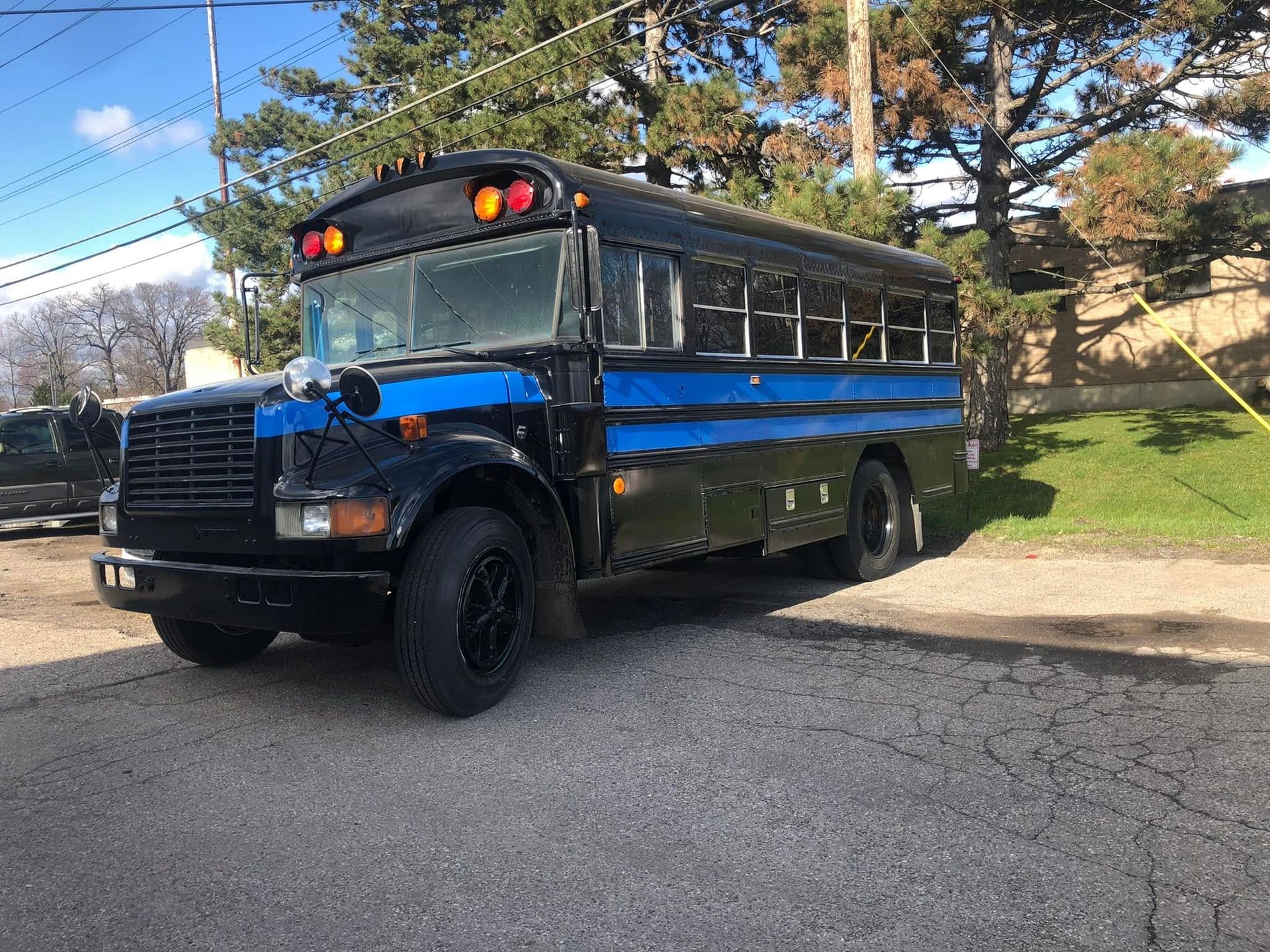 Blue and black school bus parked on a driveway beside a grassy hillside under a clear sky