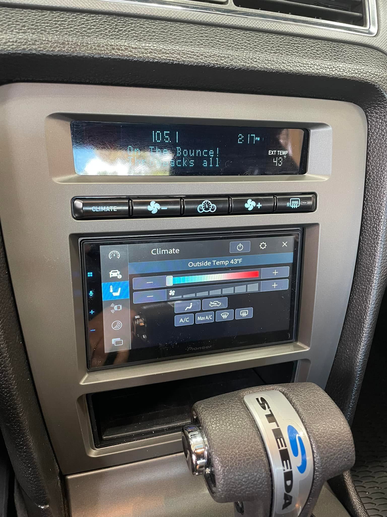 Car dashboard with touchscreen radio and climate controls, plus a gear shift knob below.