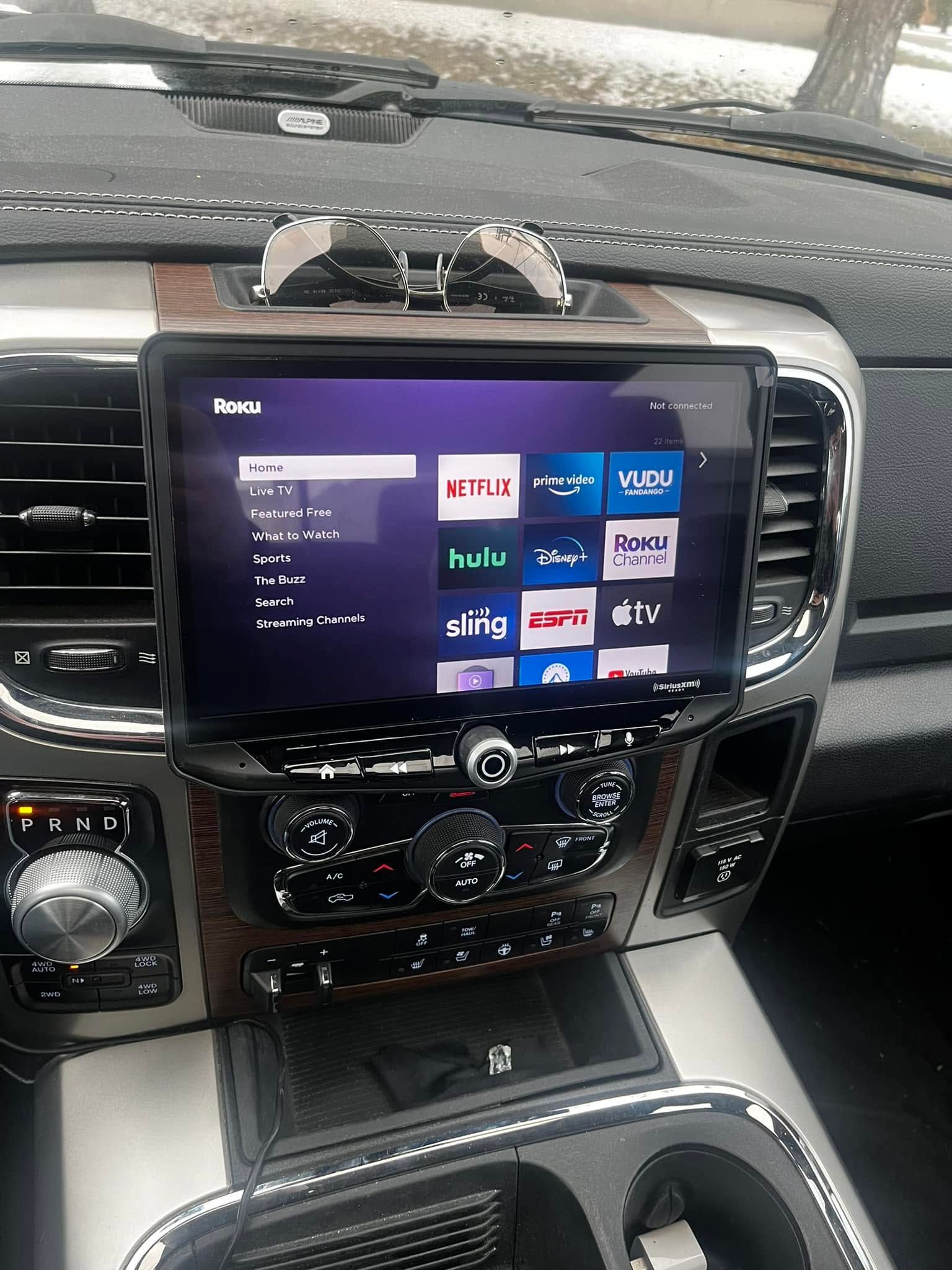 Car dashboard with a touchscreen showing the Home menu and app tiles, black and silver trim visible