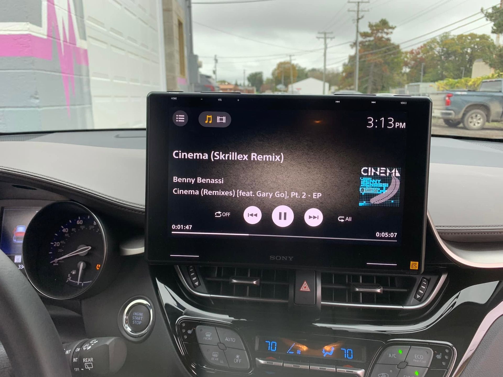 Car dashboard with infotainment screen showing music playback and climate controls.