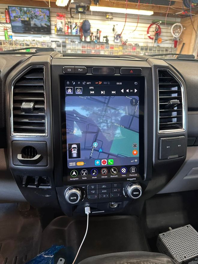 Car dashboard with a large touchscreen showing a navigation map, parked inside a garage with tools in the background